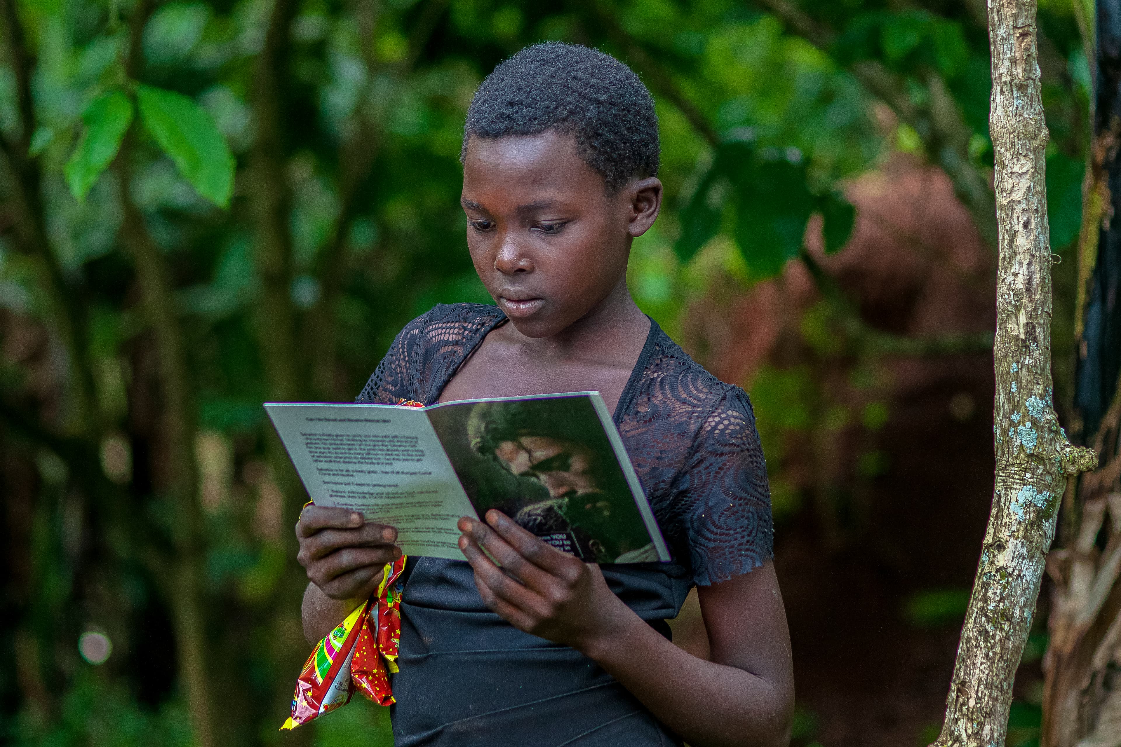 A boy reads a printed photo while holding a food gift bag outdoors.
