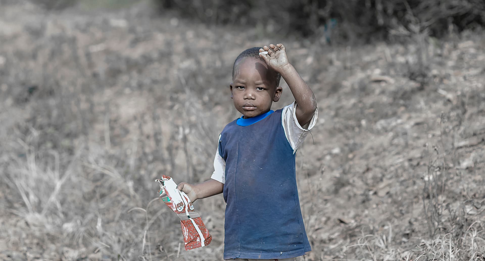 Black-and-white photo of a child raising a hand outdoors.