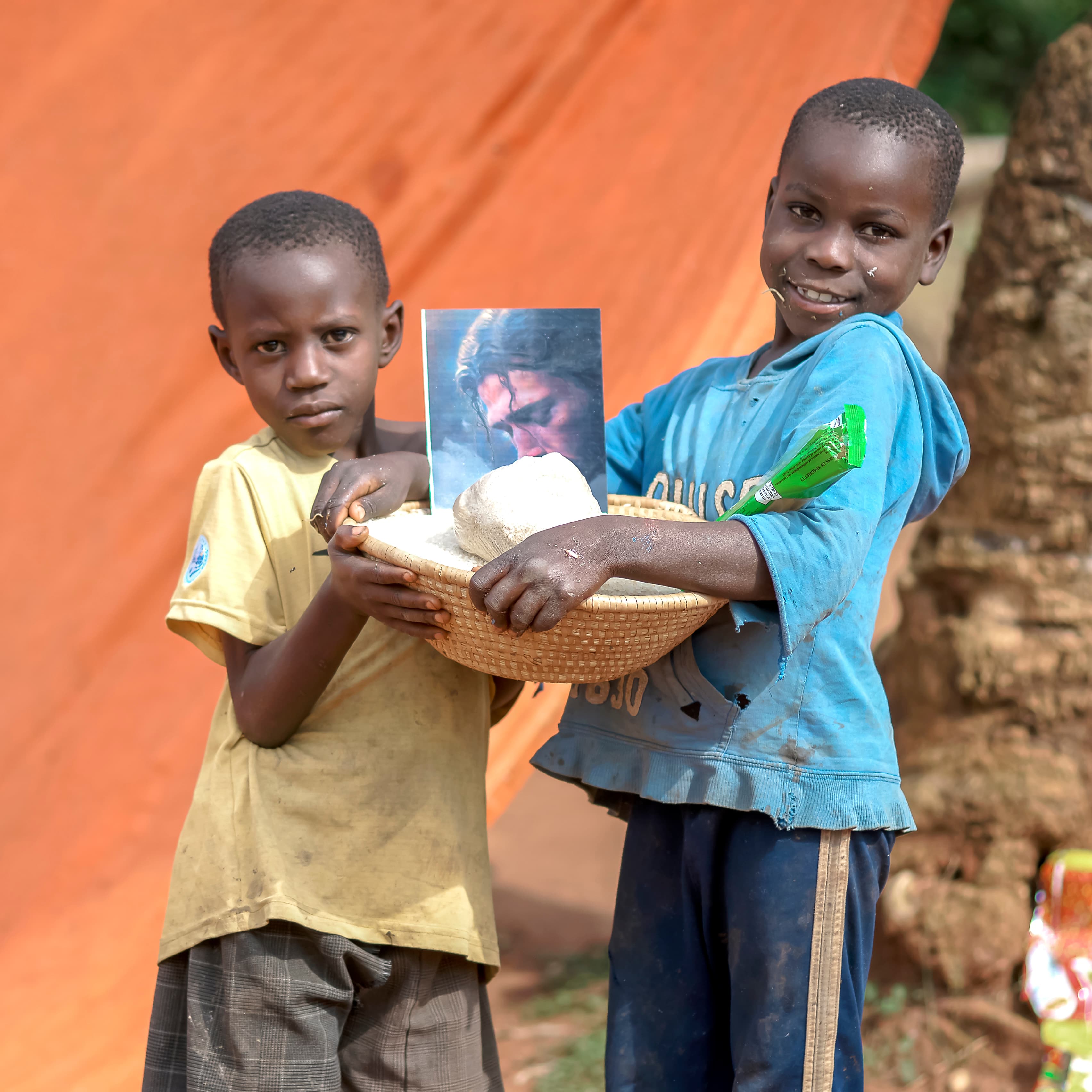 Two boys together hold a basket containing a photo and bread or food items.