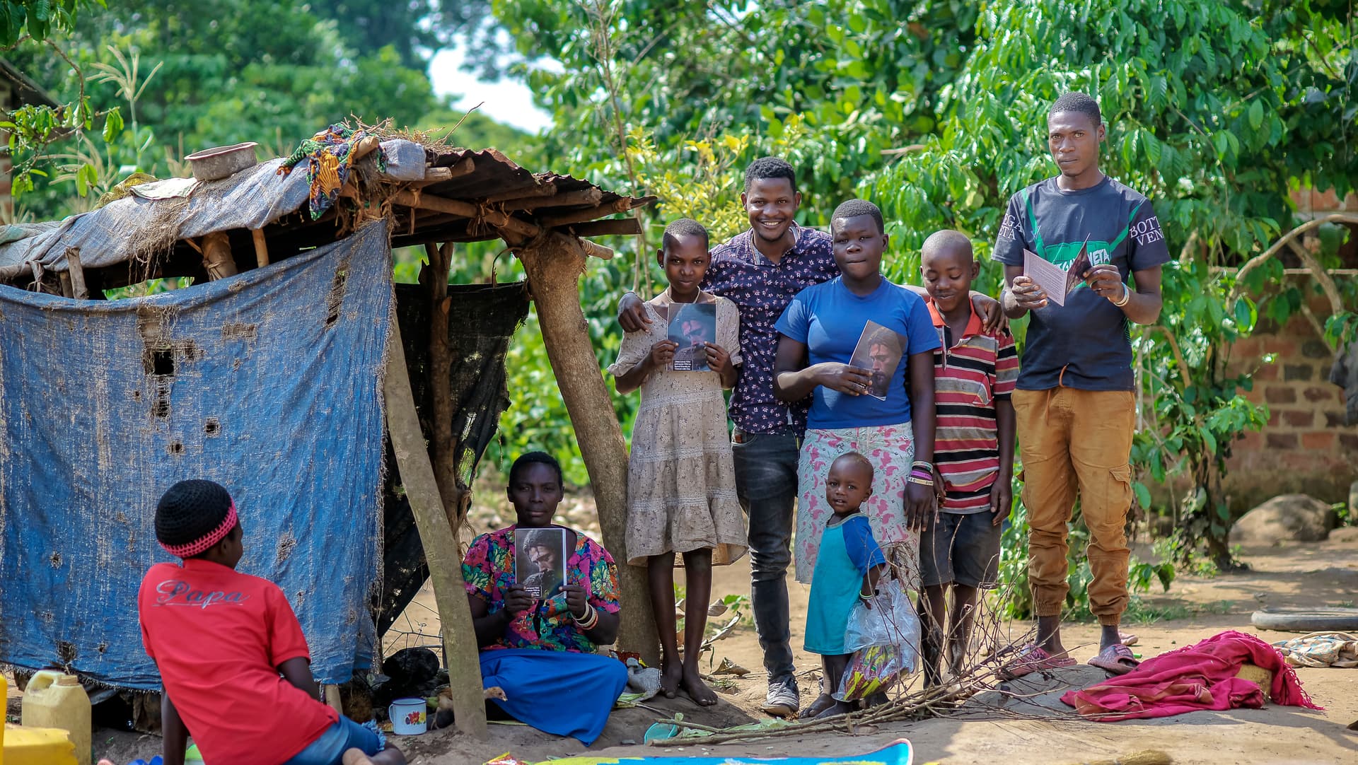 A newly saved family poses with JFM team members outdoors near a blue tarp shelter.
