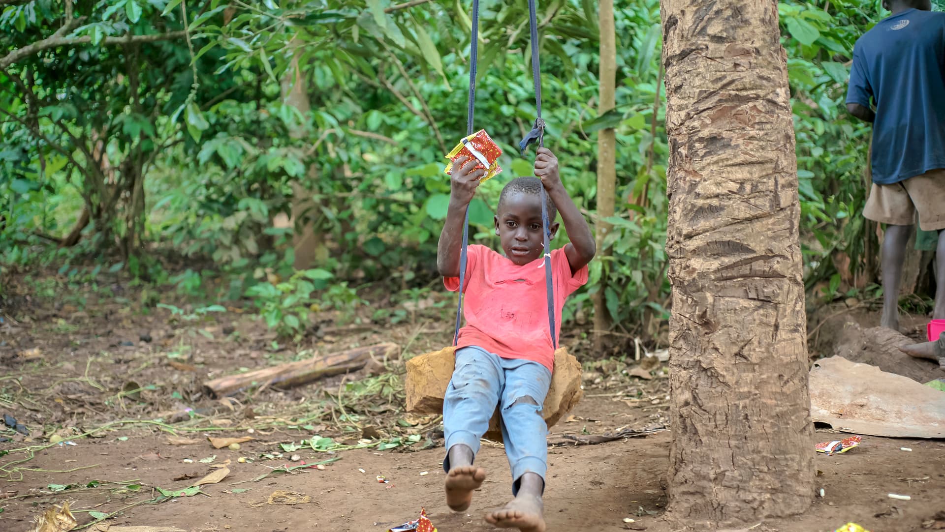 A child in a pink shirt stands near a palm tree with one hand raised.
