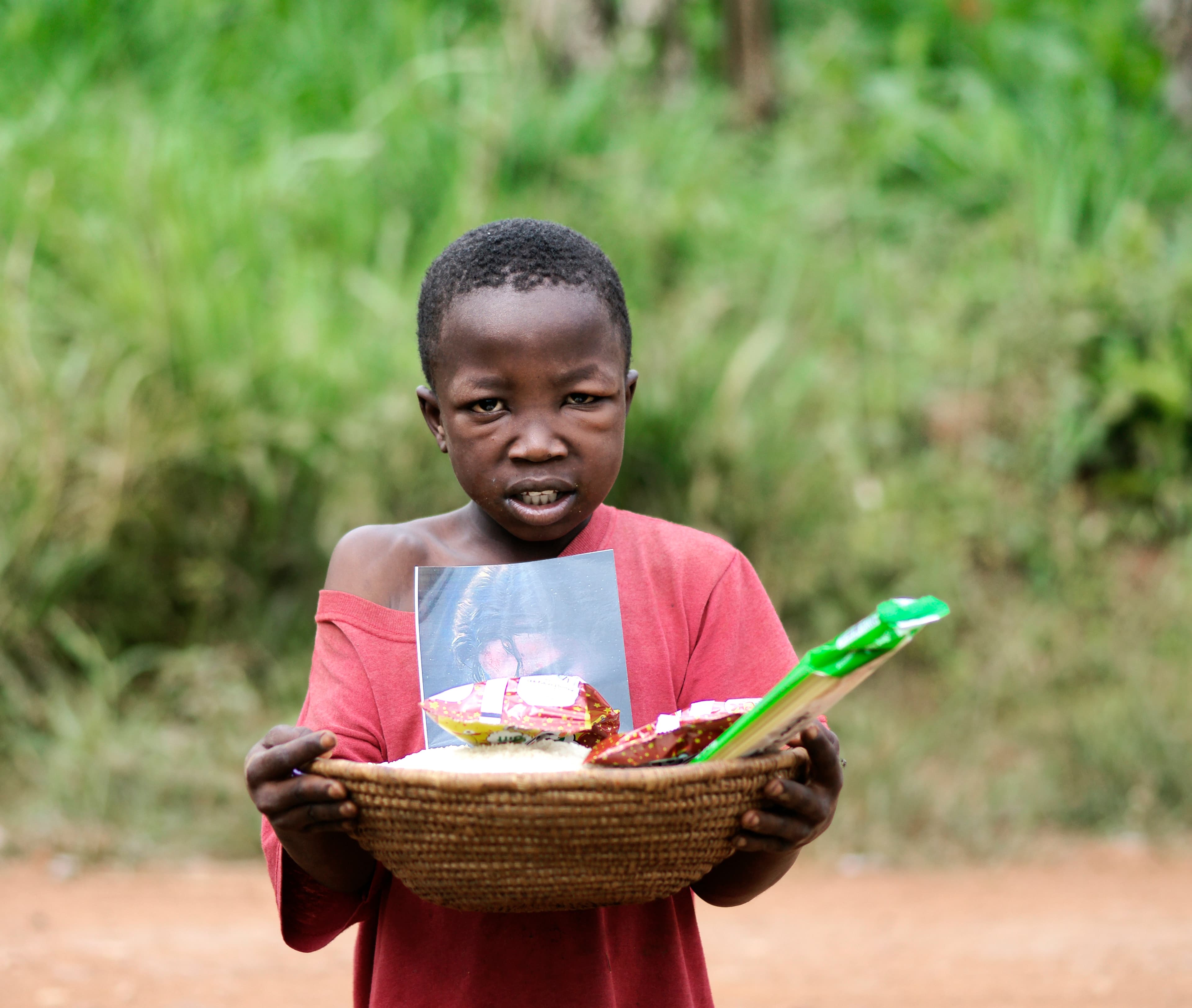 A boy holds a woven basket of food and snack items, looking toward the camera.