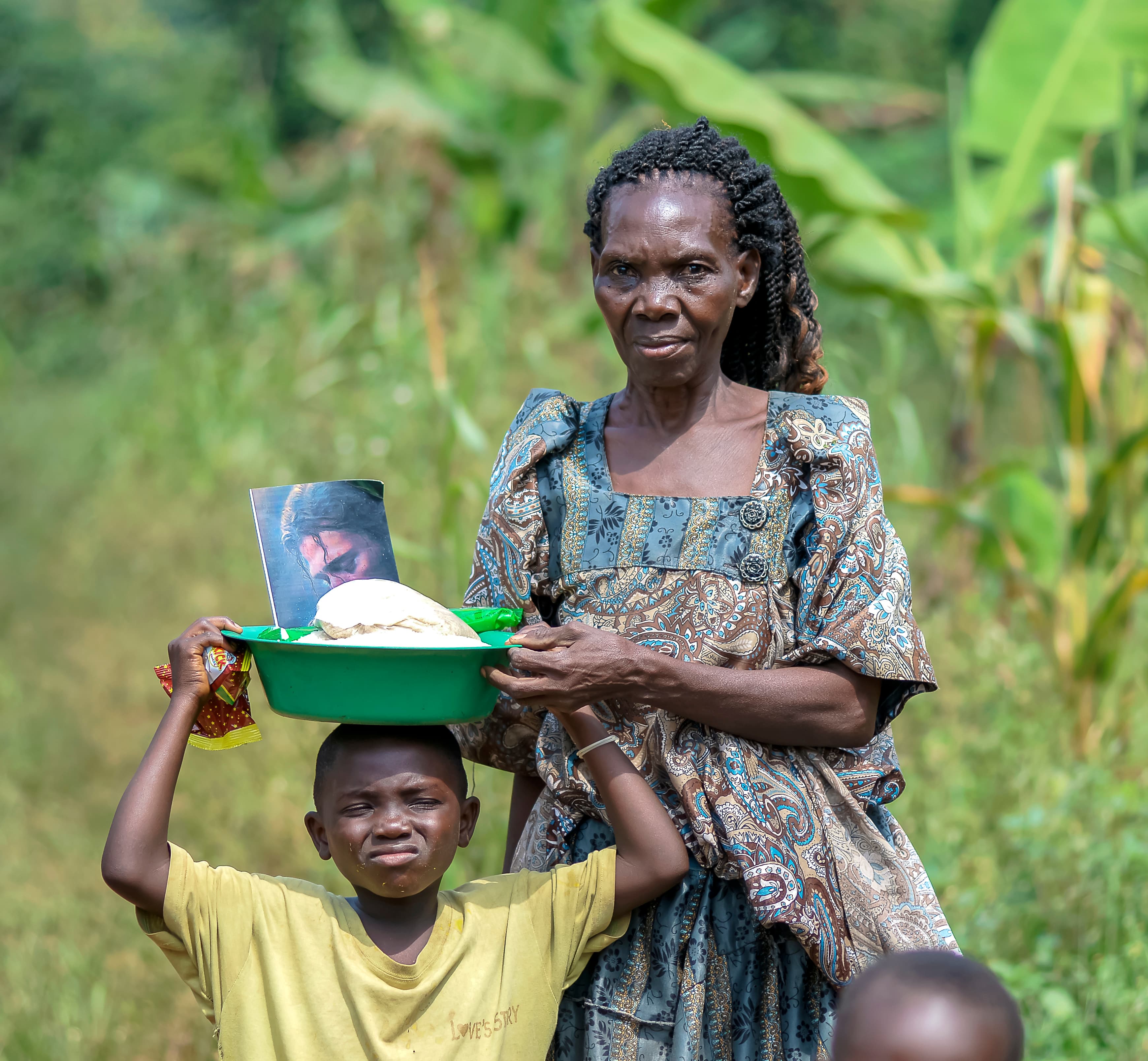 A woman and a boy hold up a framed photograph together outdoors near a food gift delivery.