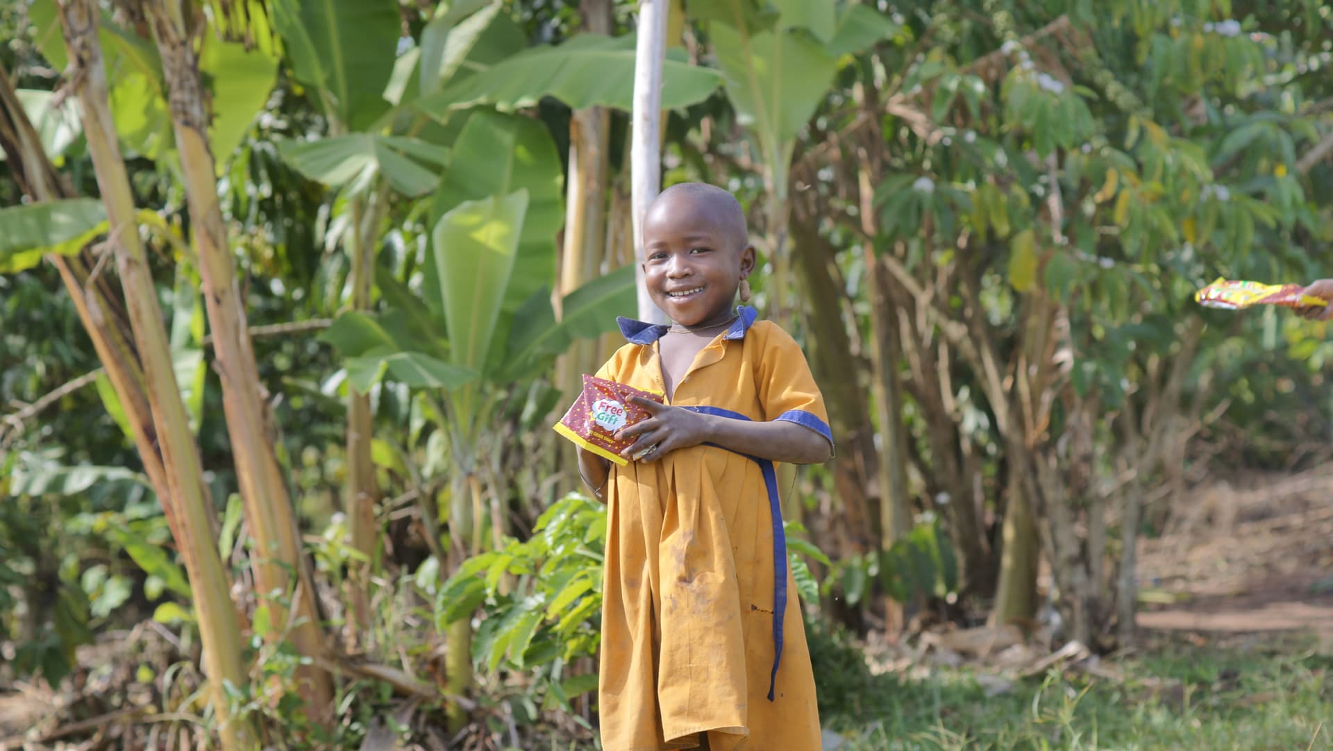 Child standing outdoors in a yellow outfit near tall grass