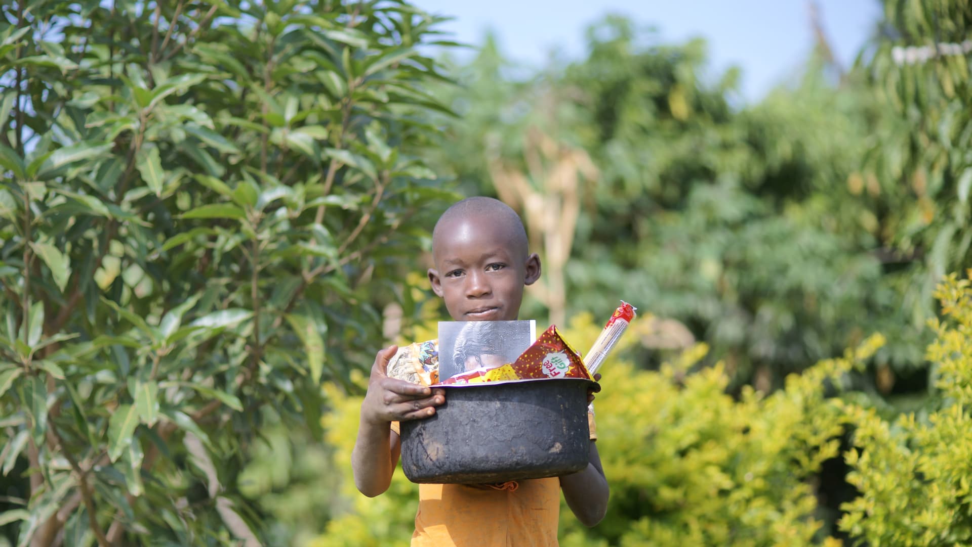 Toddler holding a black basin of food supplies outdoors