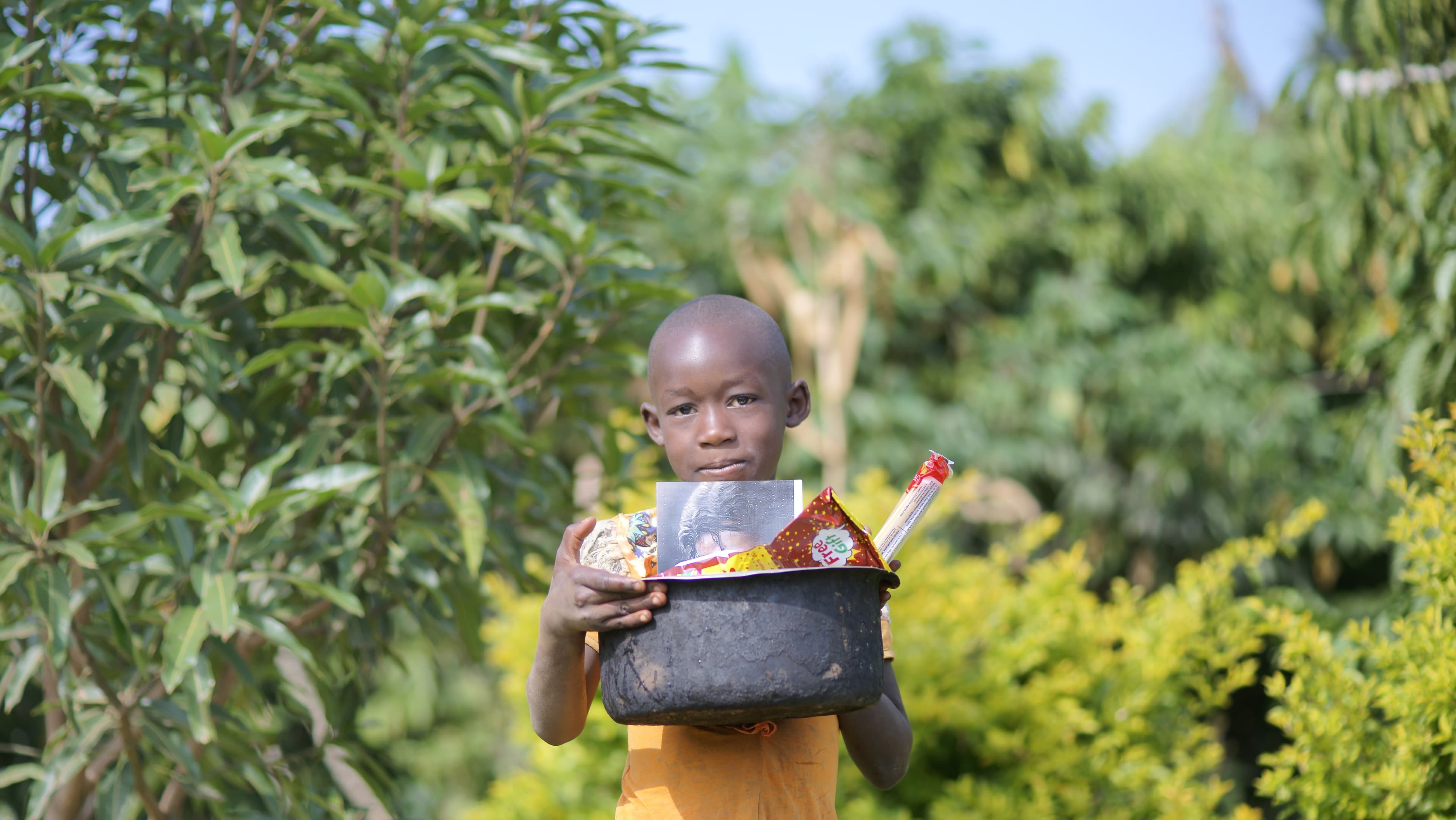 Toddler holding a black basin of food supplies outdoors