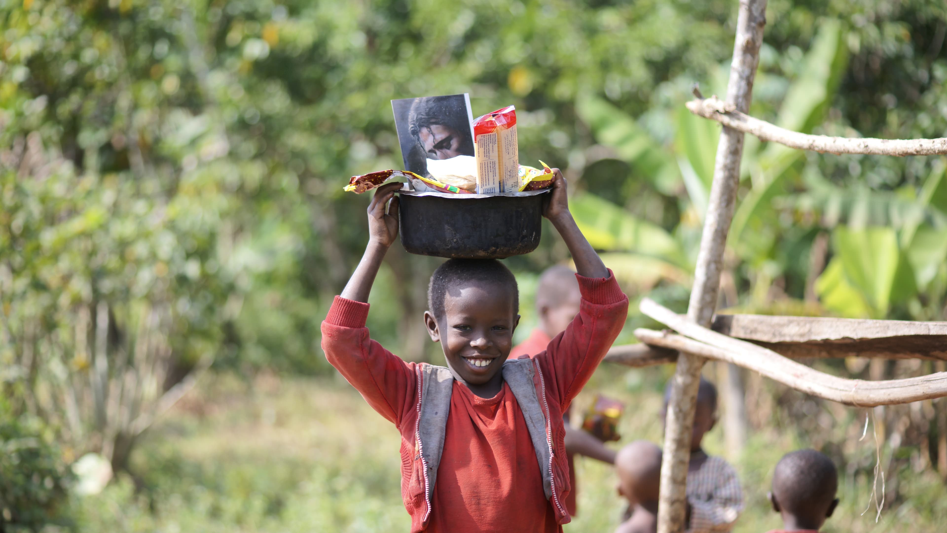 Boy carrying a black basin of food and papers on his head outdoors