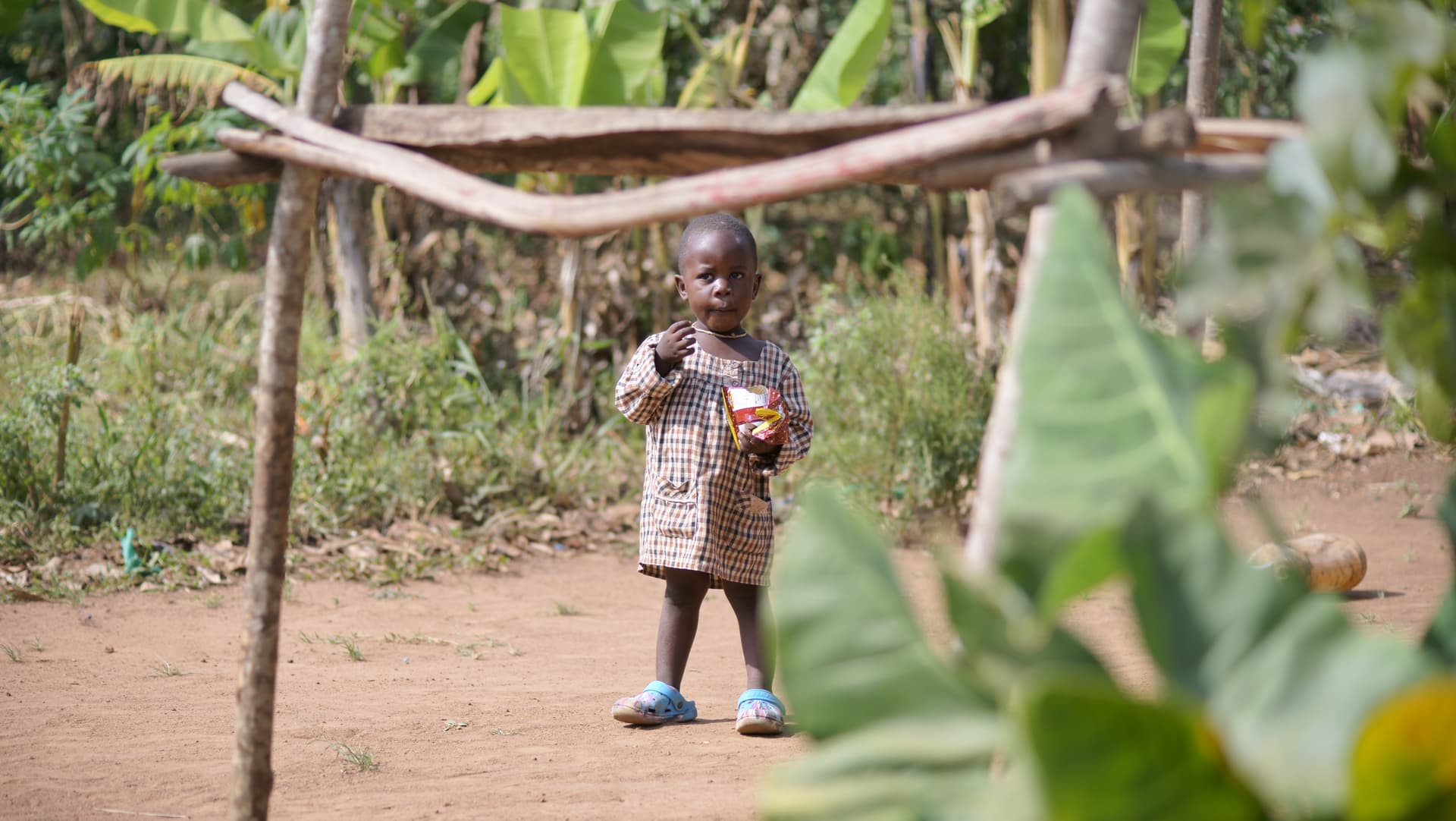 Small child standing alone on a dirt path near a wooden structure