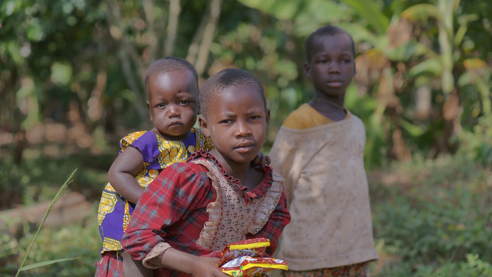 Group of children standing together outdoors, one holding a food item