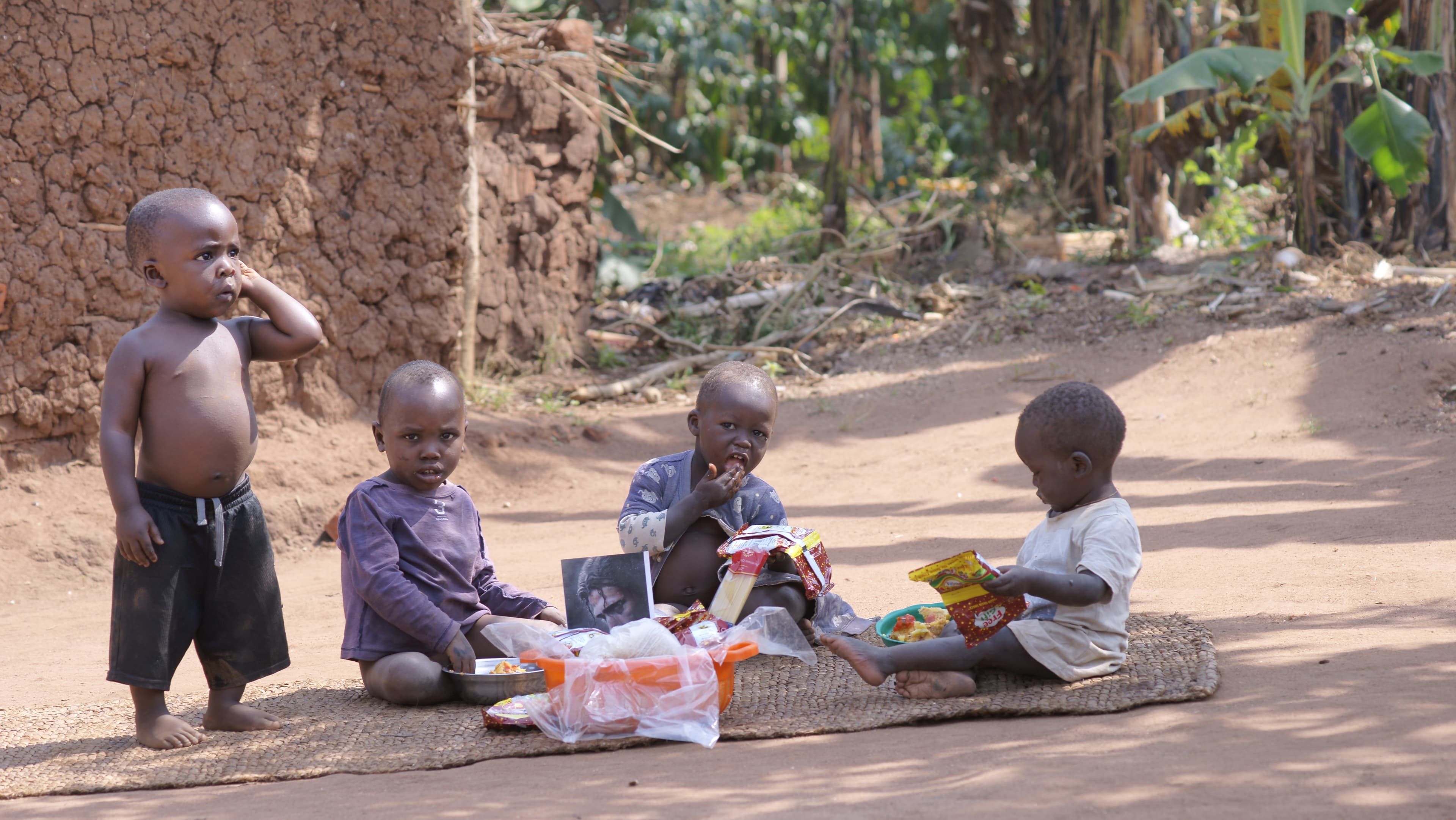 Children sitting together outdoors with bowls of food spread out before them