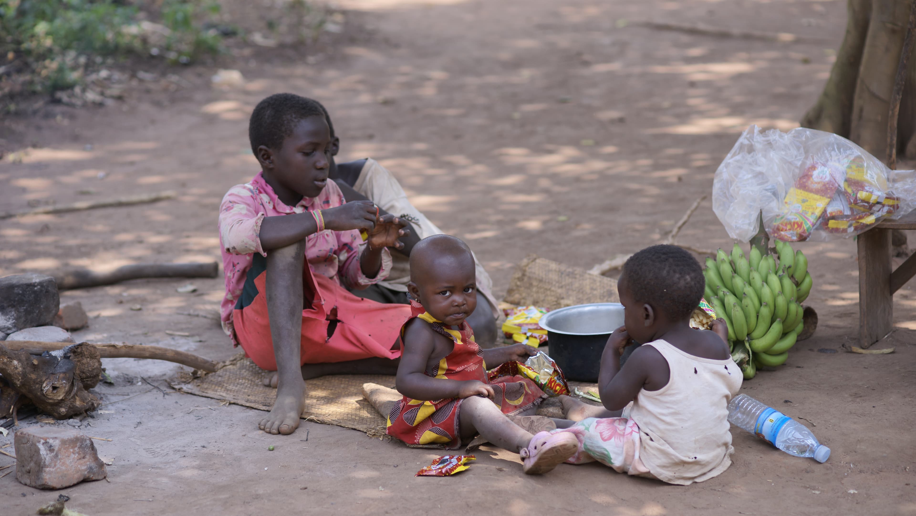 Group of children sitting together outdoors sharing food and bananas