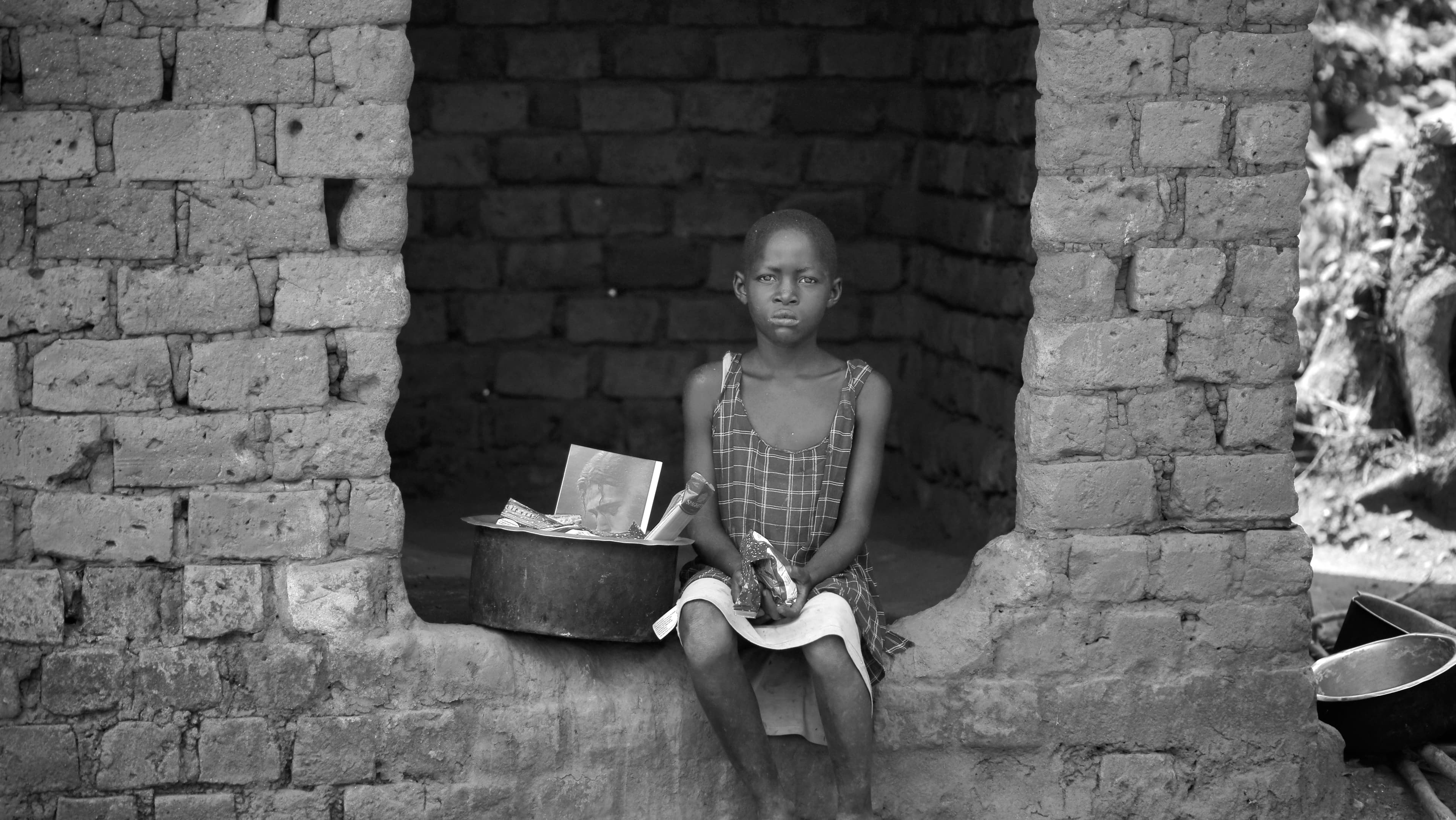 Black and white image of a young girl sitting outdoors near a metal basin