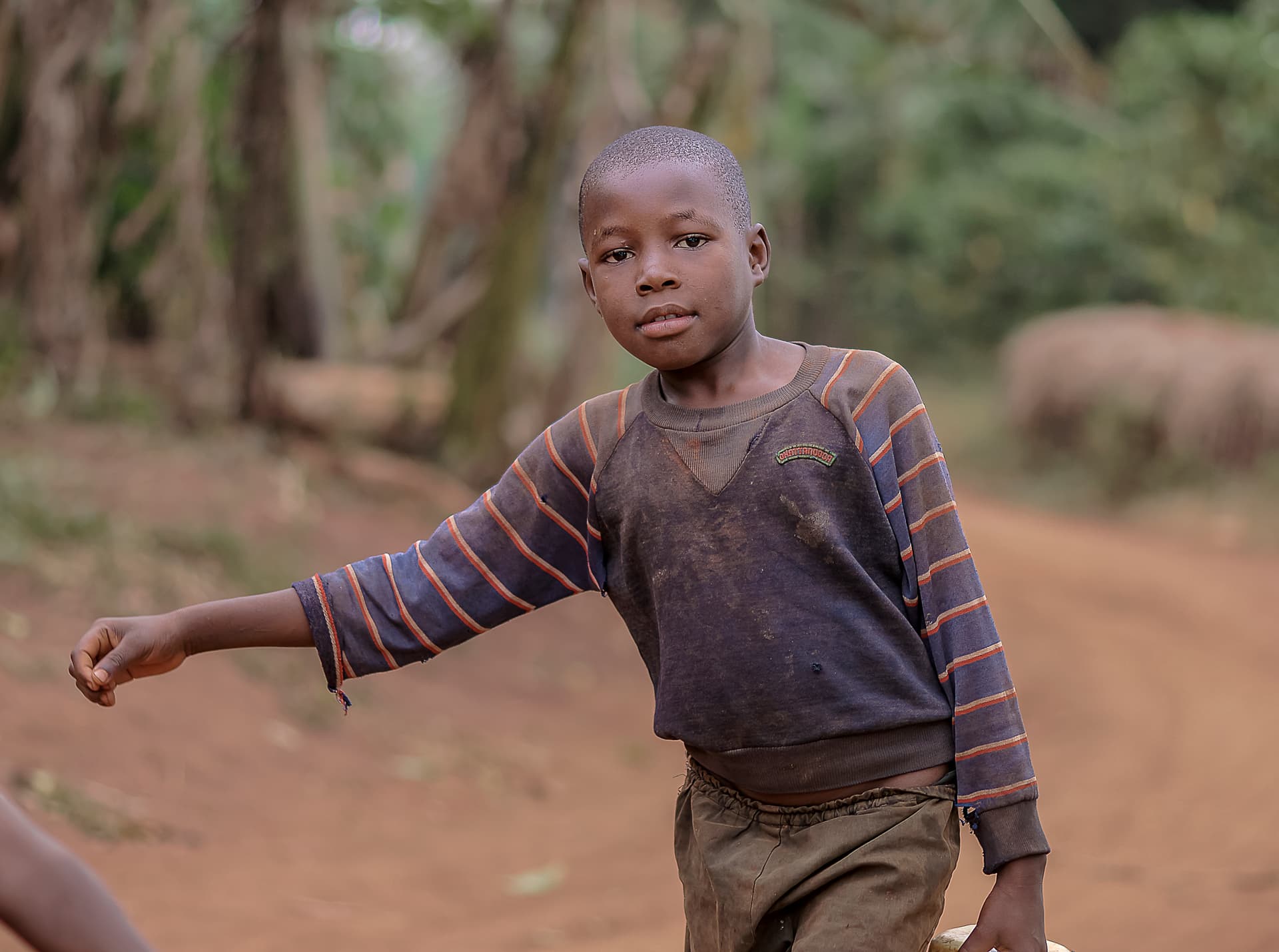 Boy gesturing with his hand while standing on a dirt path