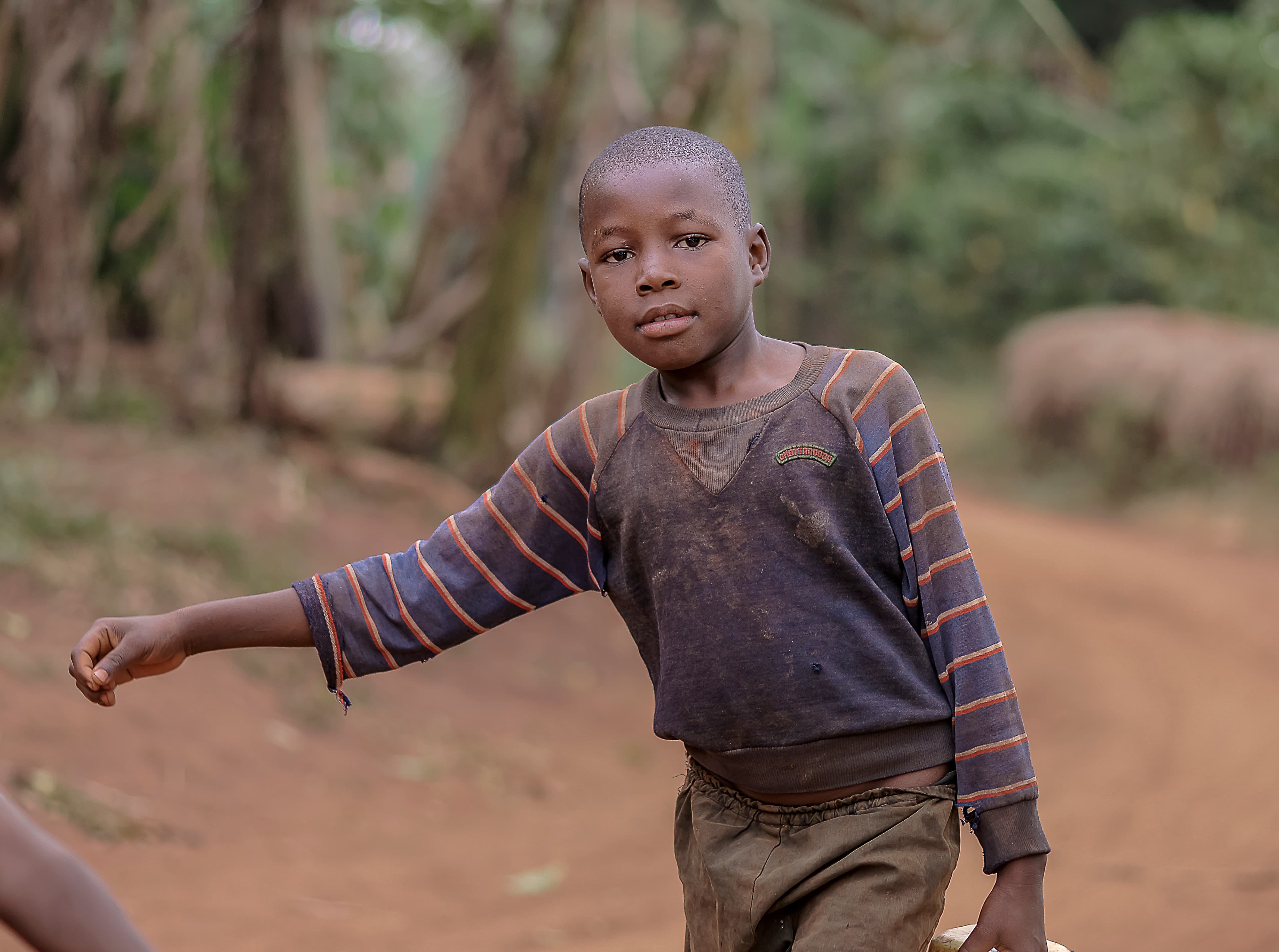 Boy gesturing with his hand while standing on a dirt path