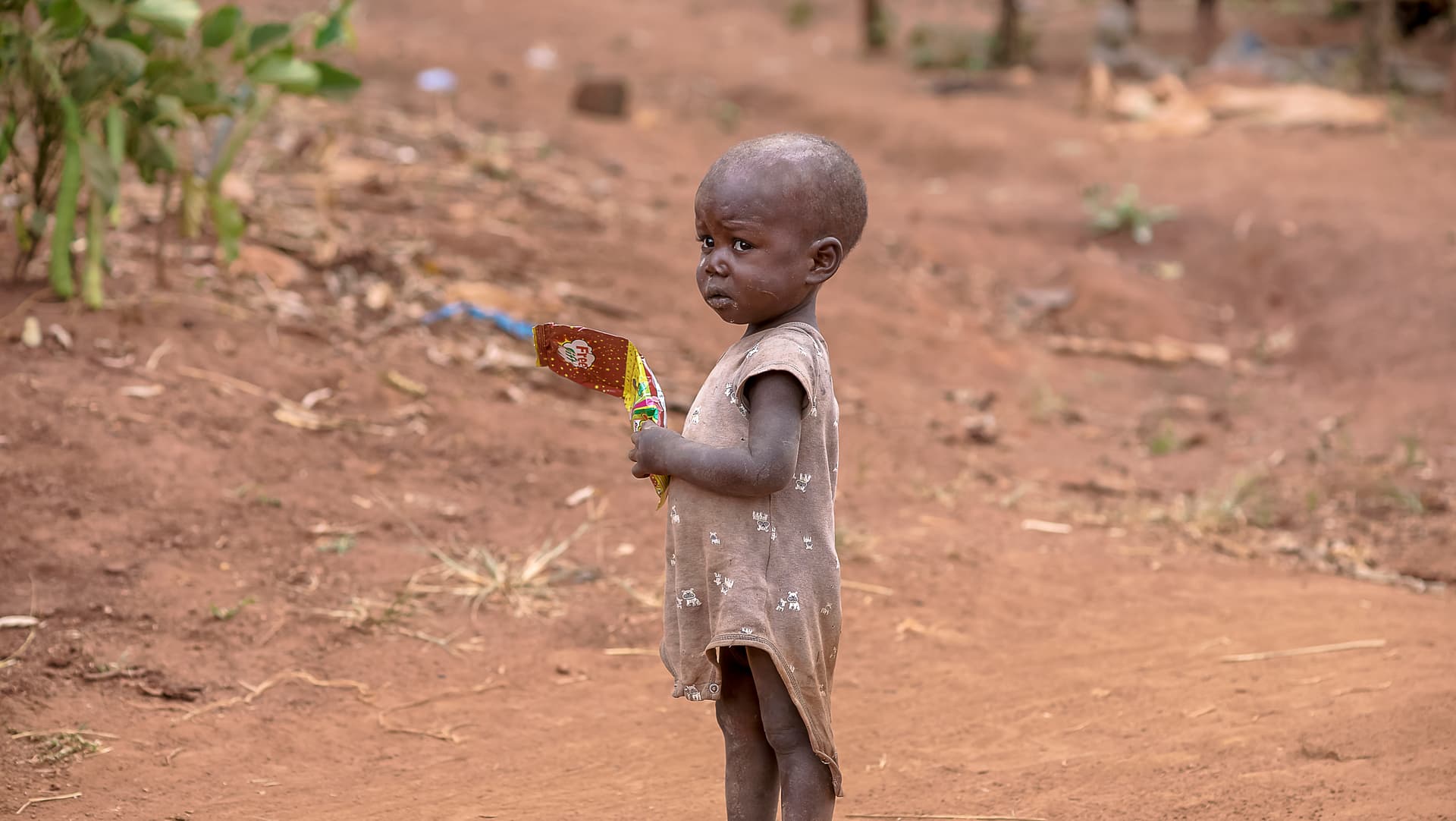 Small child standing alone outdoors holding a small item