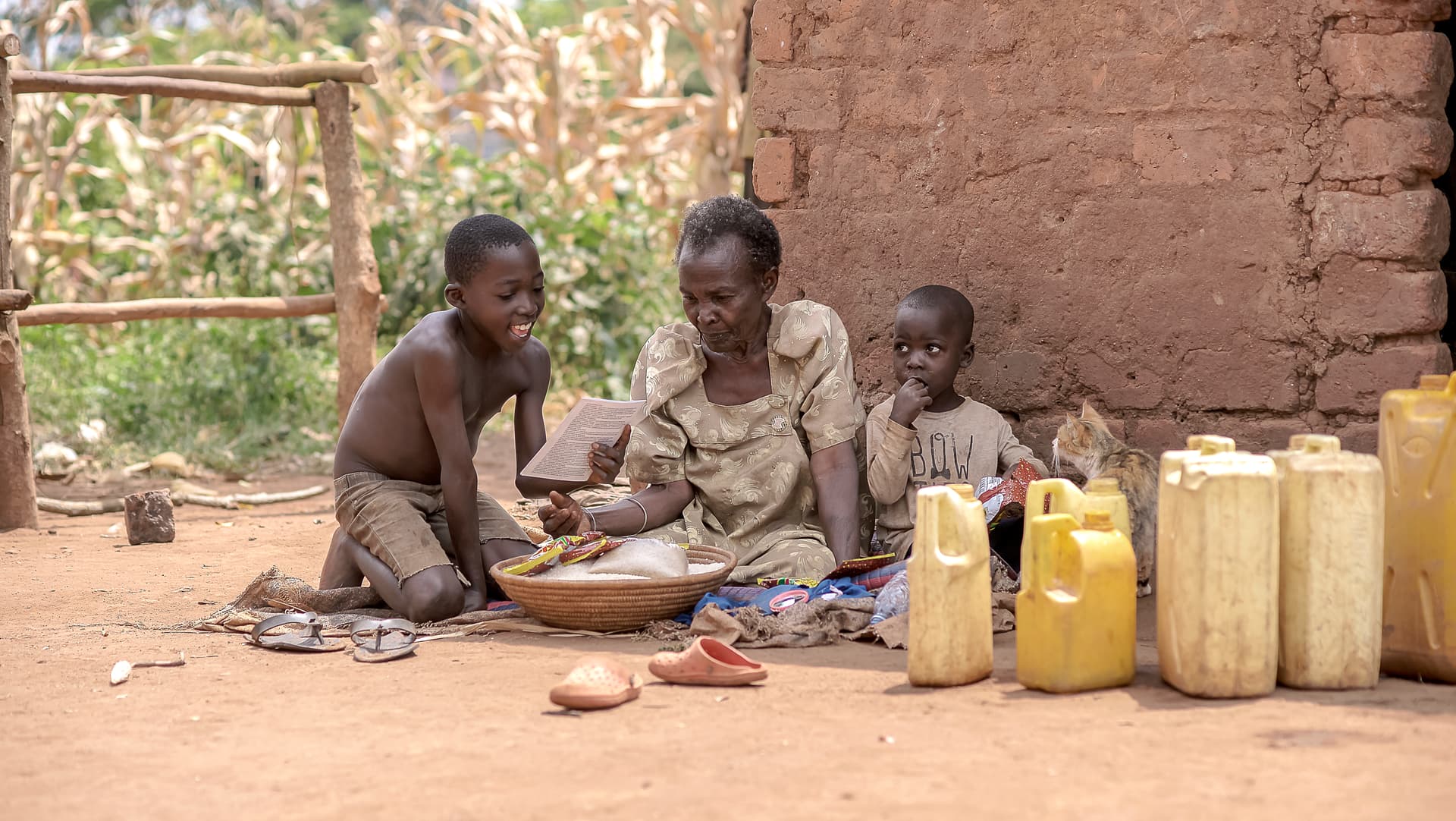 Elderly woman and a child sitting outdoors on the ground beside yellow jerry cans