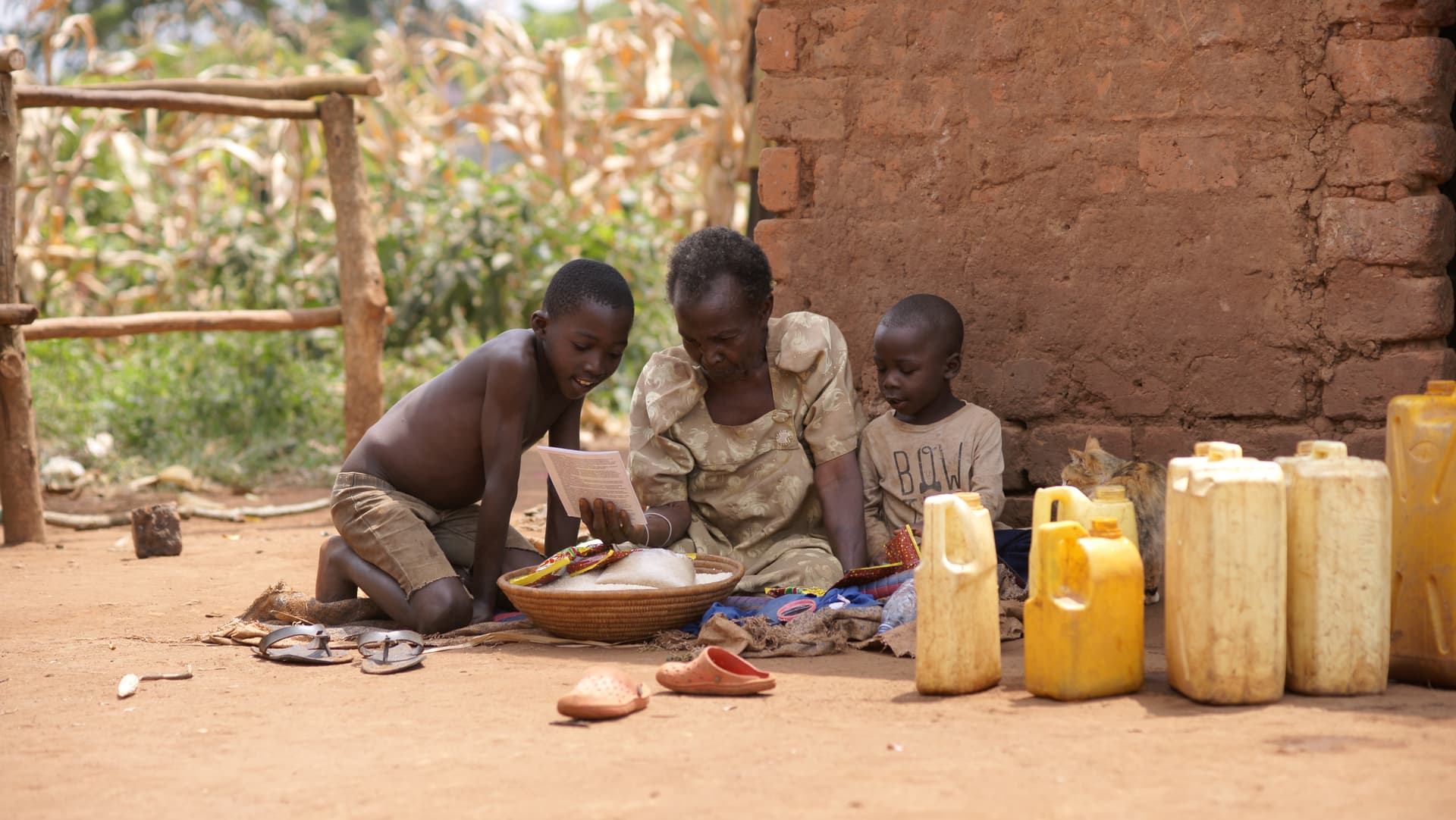 Elderly woman and children sitting outdoors with yellow jerry cans, engaged in a task