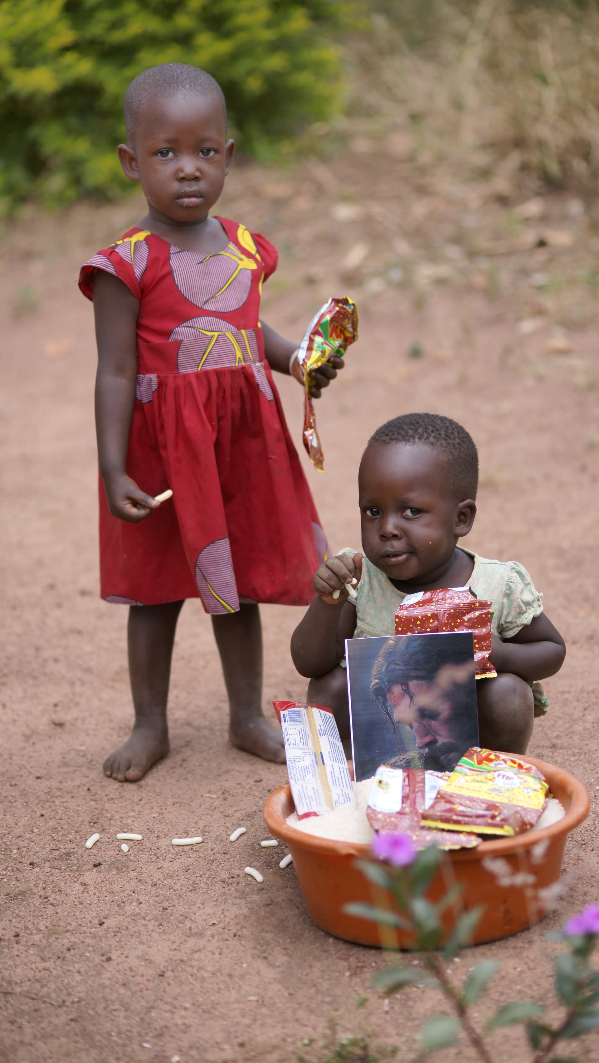 Girl in a red dress lying on the ground beside a boy, both looking at the camera