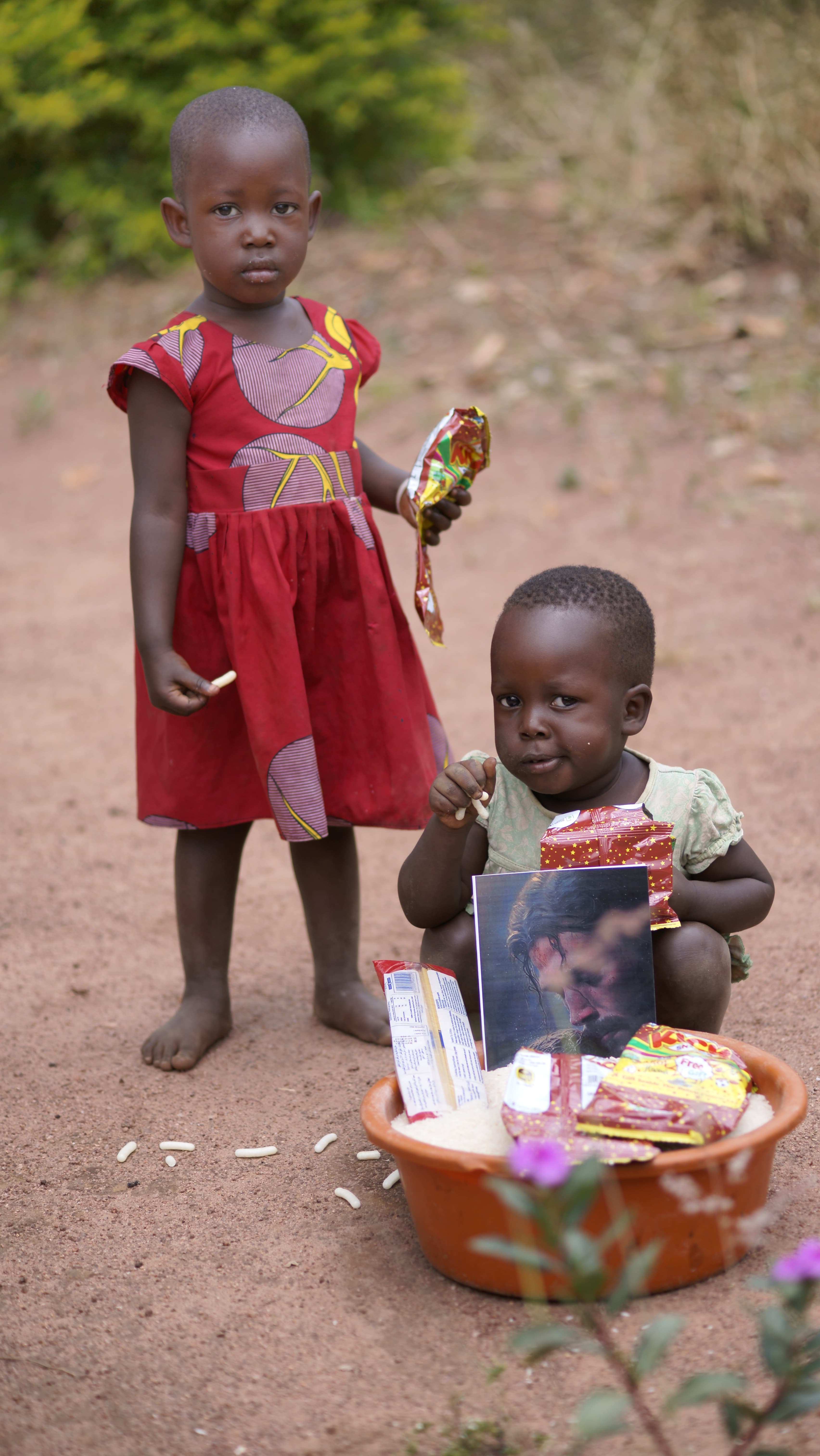 Girl in a red dress lying on the ground beside a boy, both looking at the camera