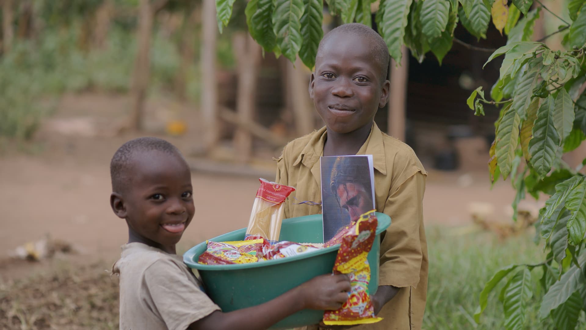 Smiling boy holding a teal basin of food supplies and a photo card