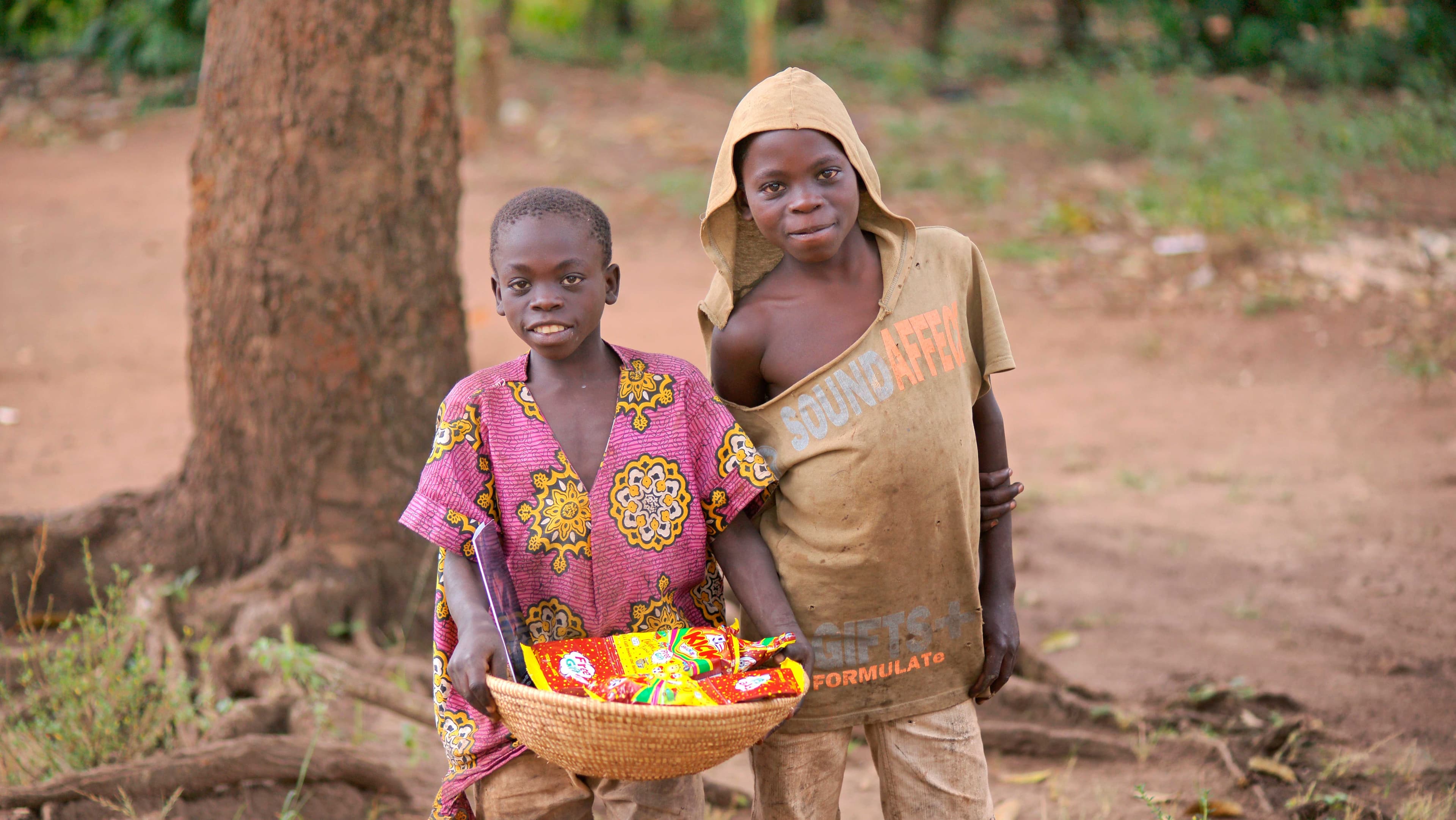 Woman and child standing outdoors holding a basket of food items, different angle