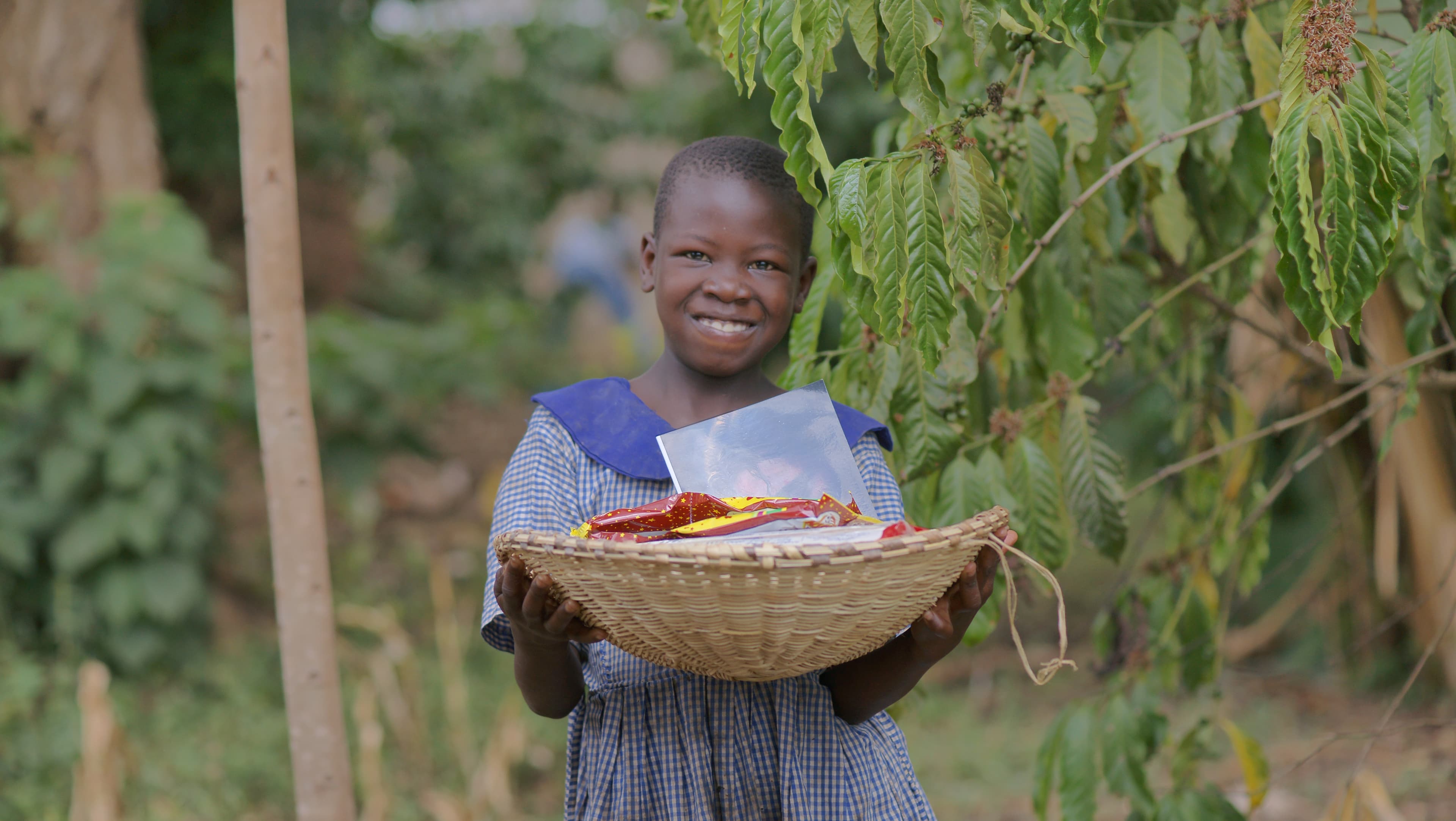 Girl smiling while carrying a basket of food items outdoors among greenery