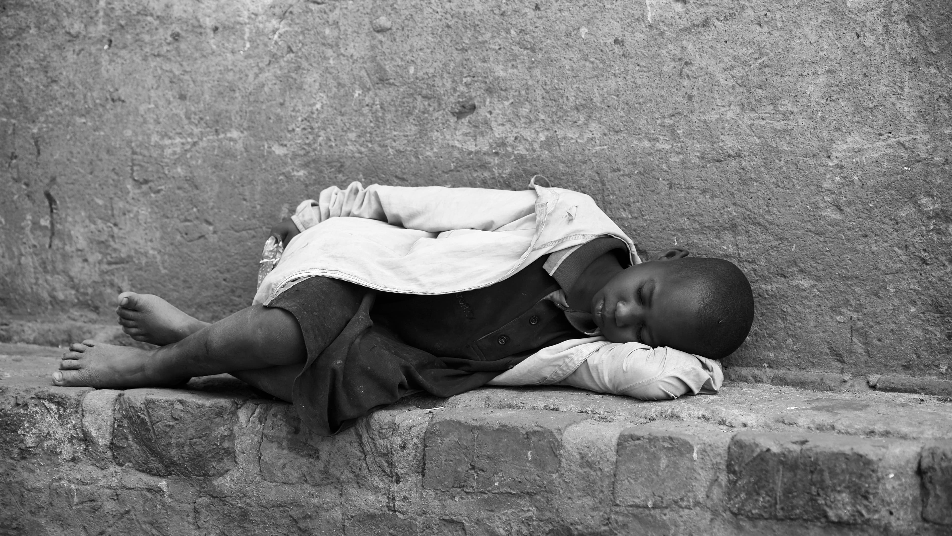 Black and white image of a child lying on a brick ledge, appearing to sleep