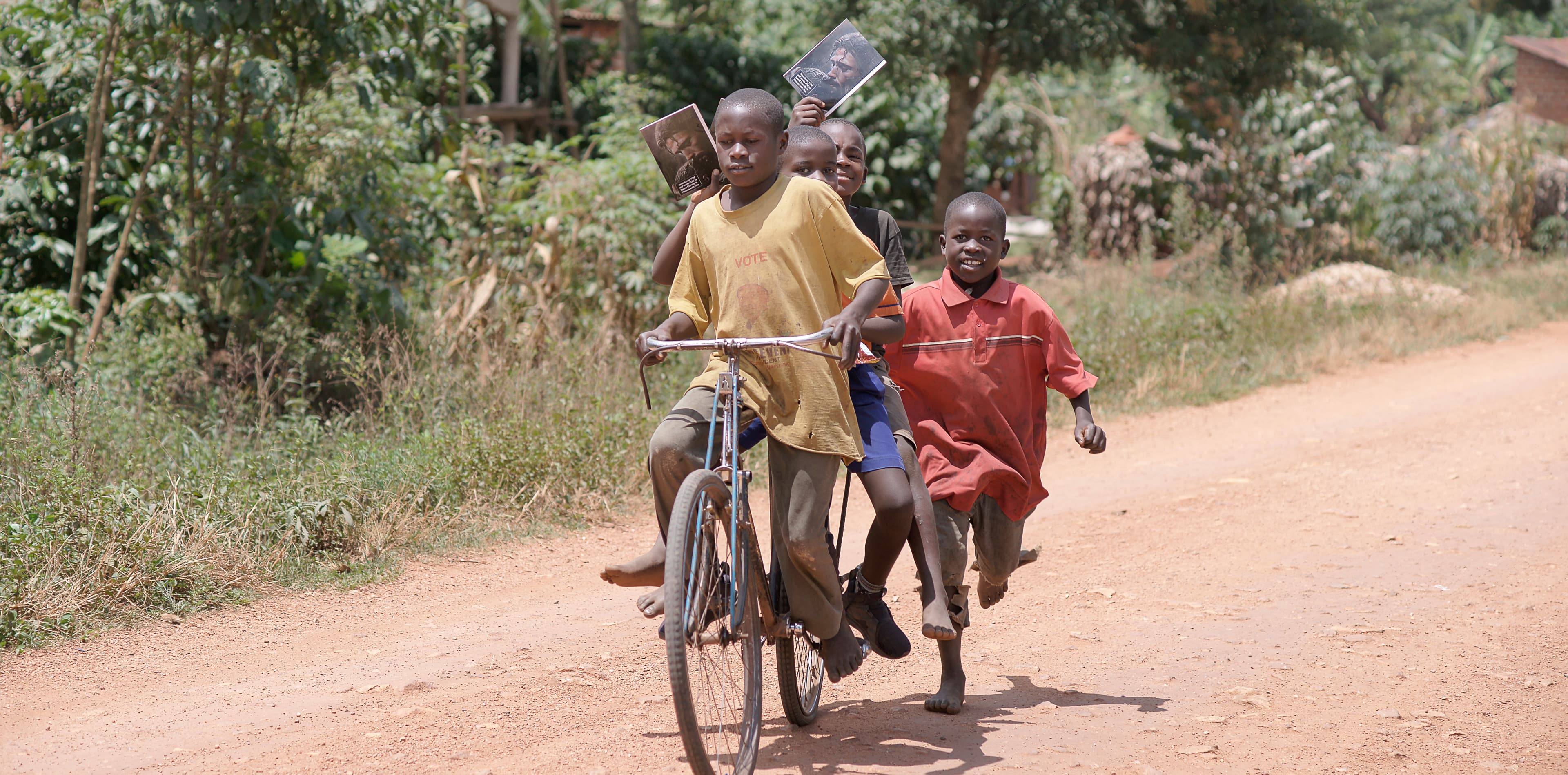 Two boys riding a bicycle together down a dirt road