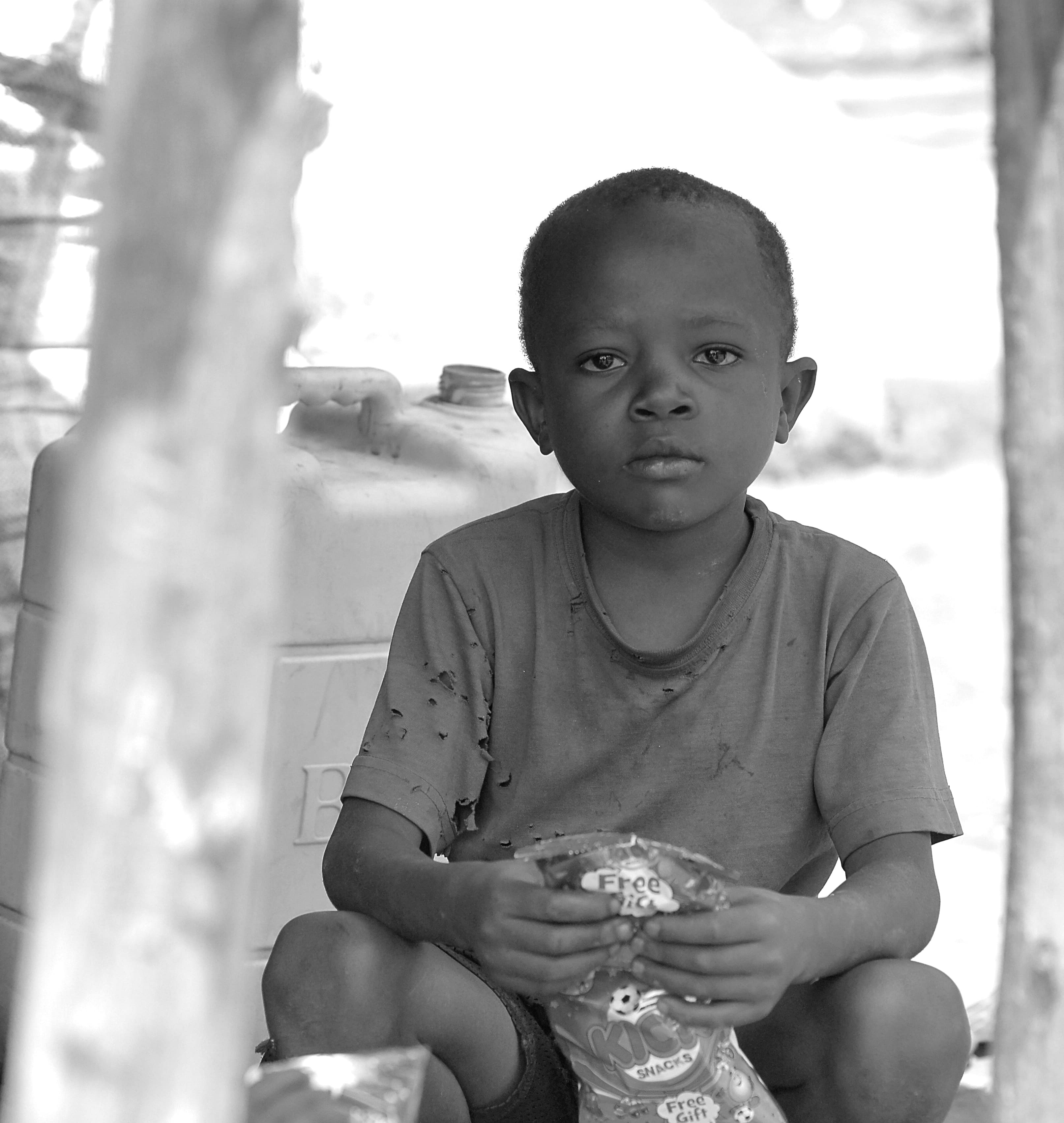 Black and white close-up of a young child crouching outdoors, holding an item in their hands