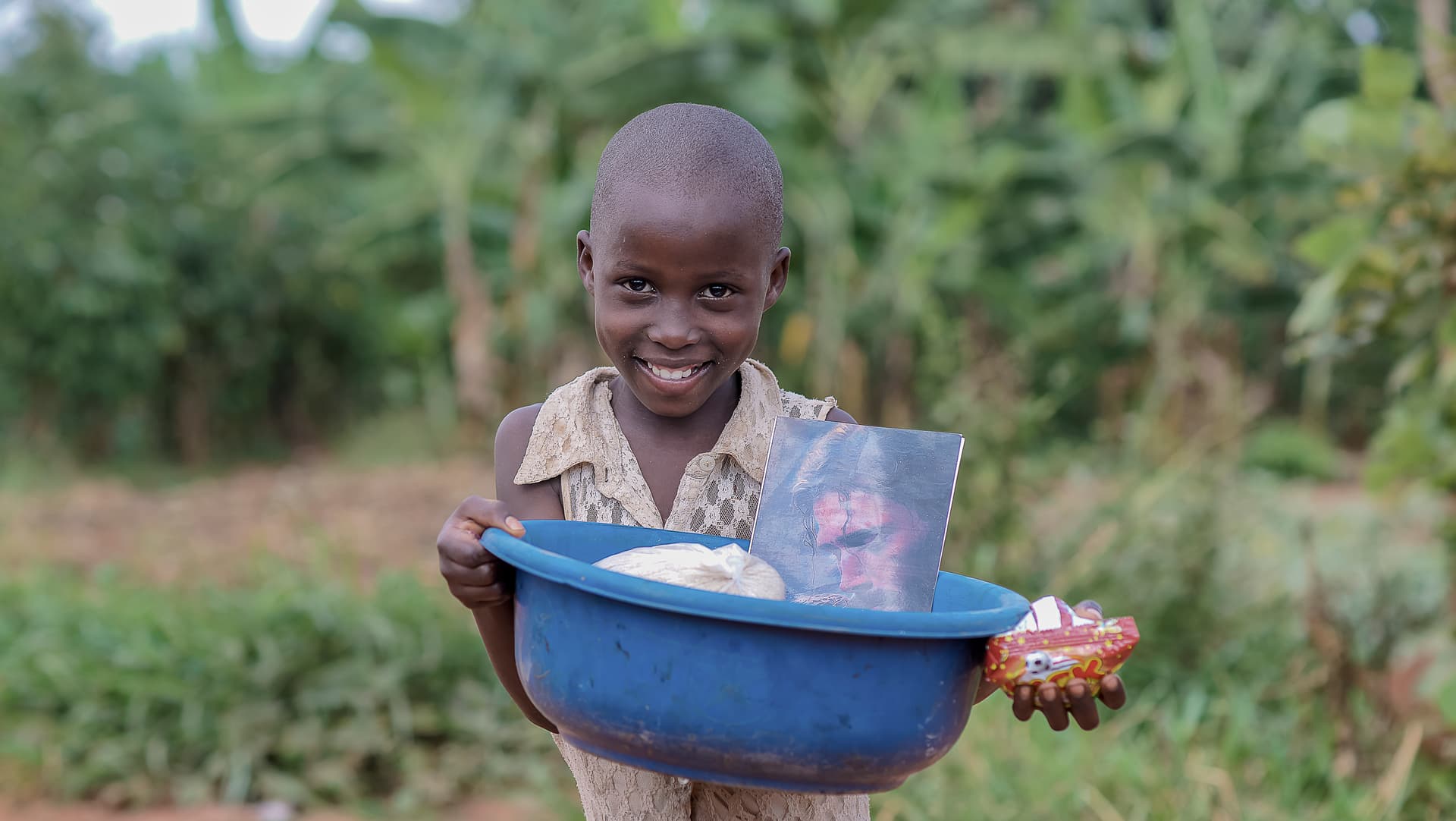 Smiling boy carrying a blue basin of food supplies on his head outdoors