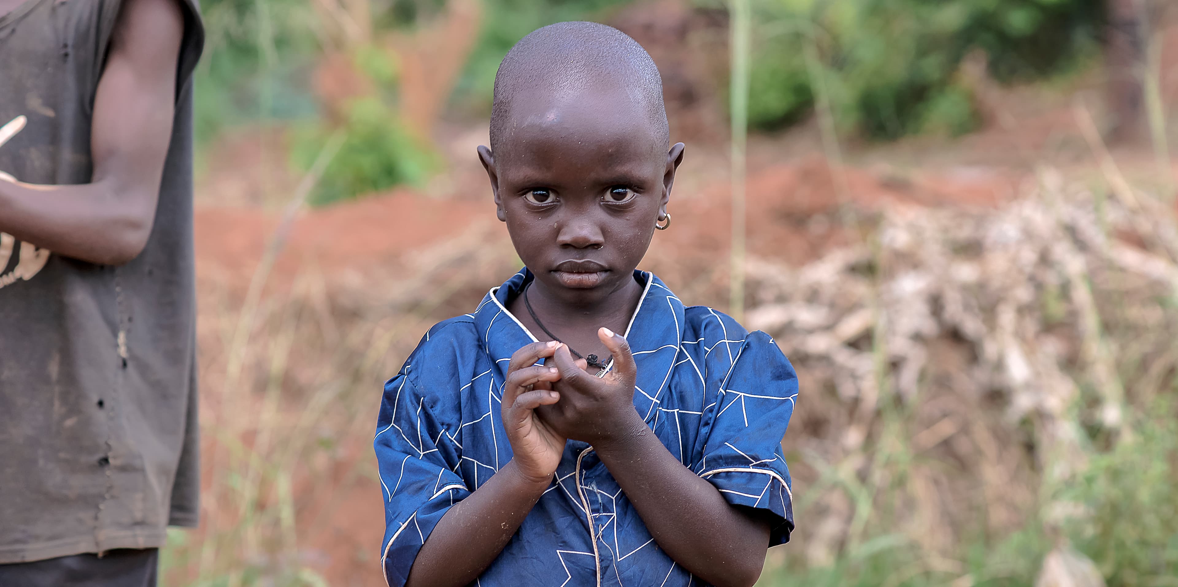 Child in a blue shirt standing outdoors with hands clasped together