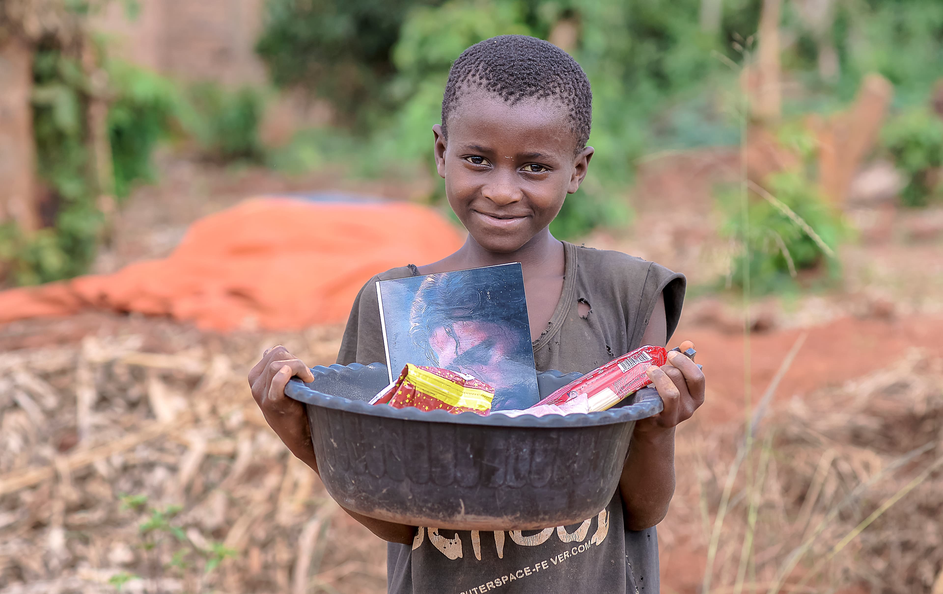 Smiling boy carrying a black basin of food supplies on his head near a food distribution