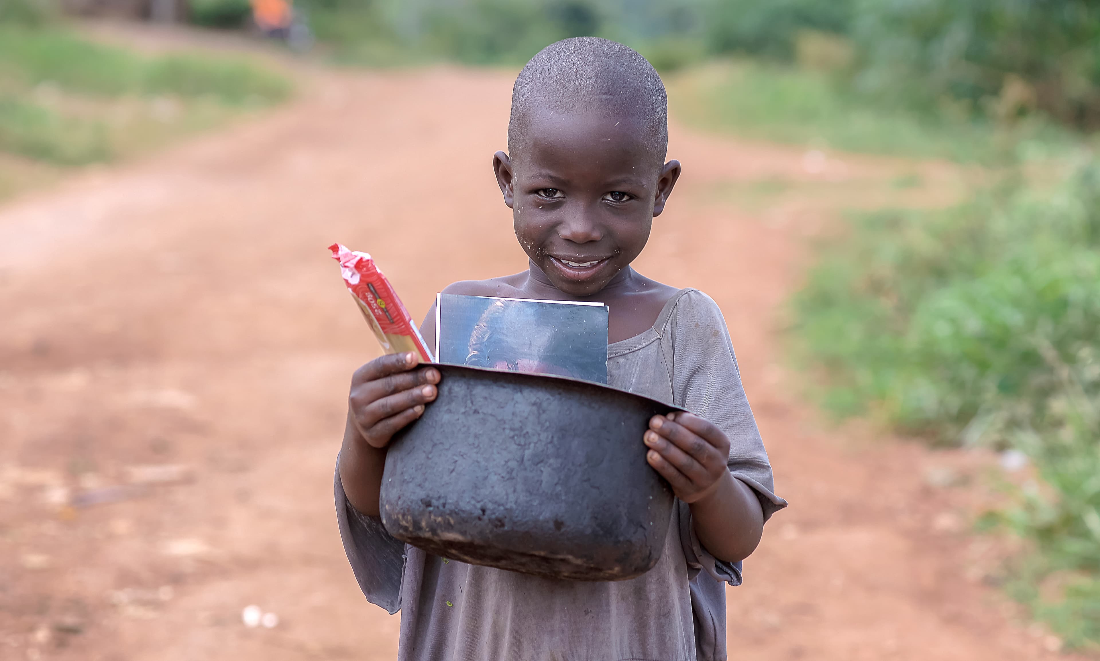 Boy carrying a black basin of food packets on his head along a rural road