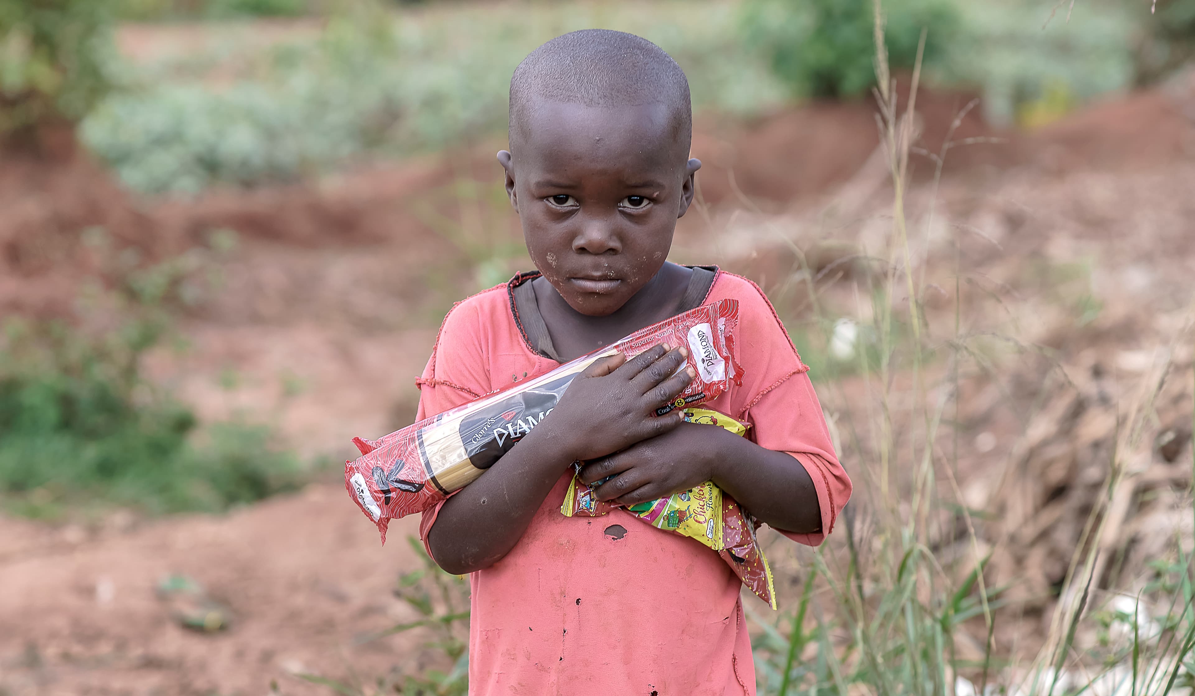 Young child in a pink shirt clutching a food packet close to their chest