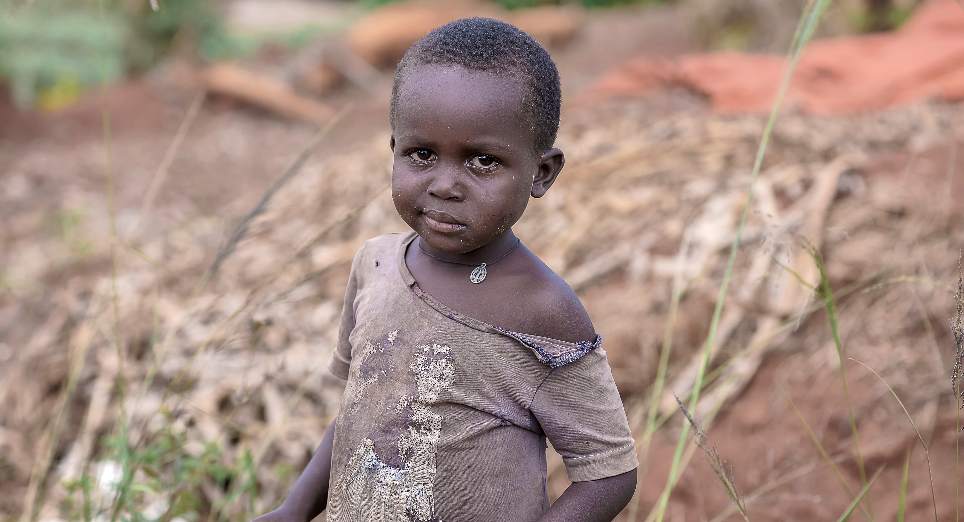 Young child standing alone on a dirt path with hands clasped together