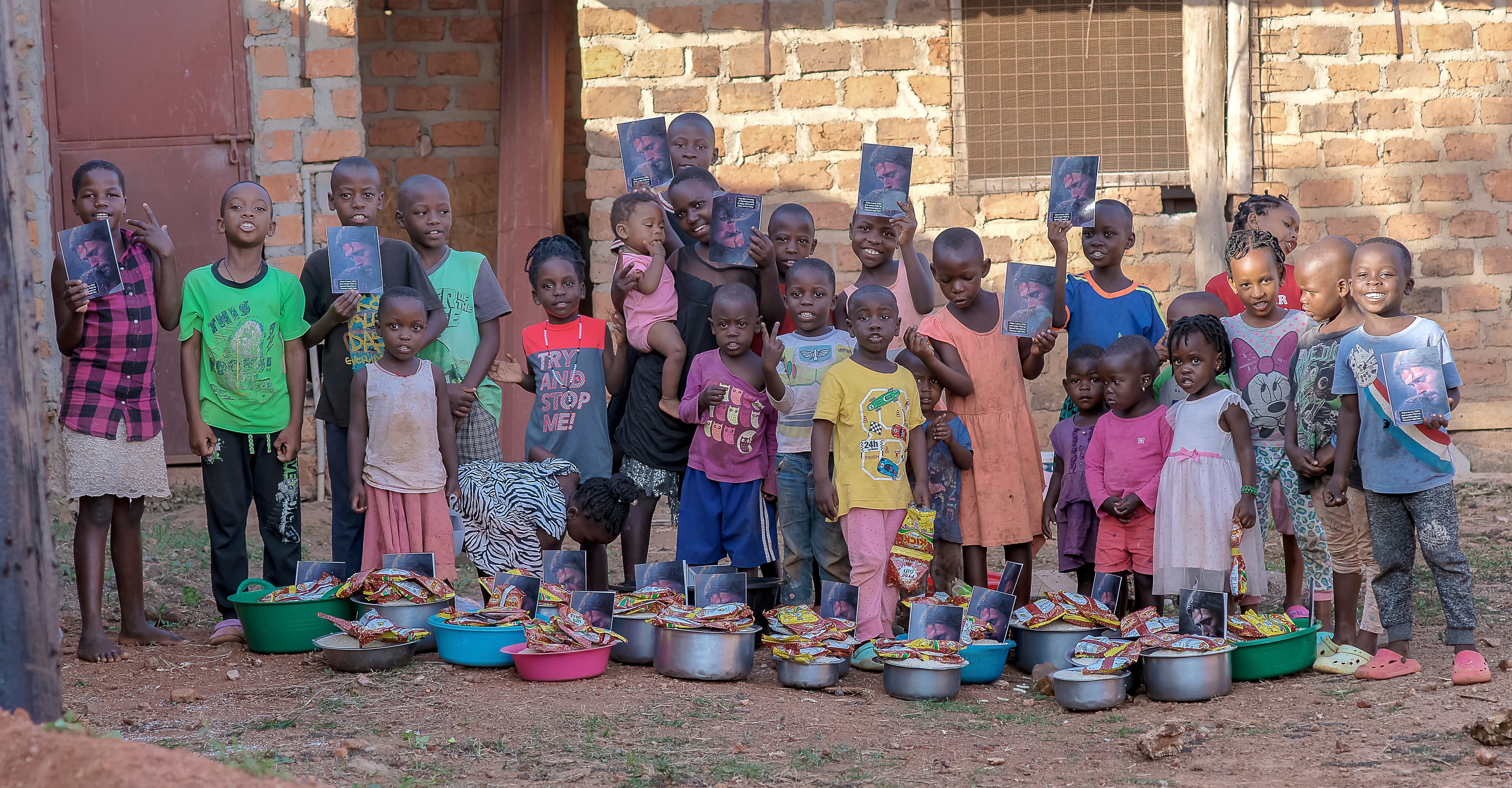 Line of children standing against a brick wall with food bowls set on the ground in front of them
