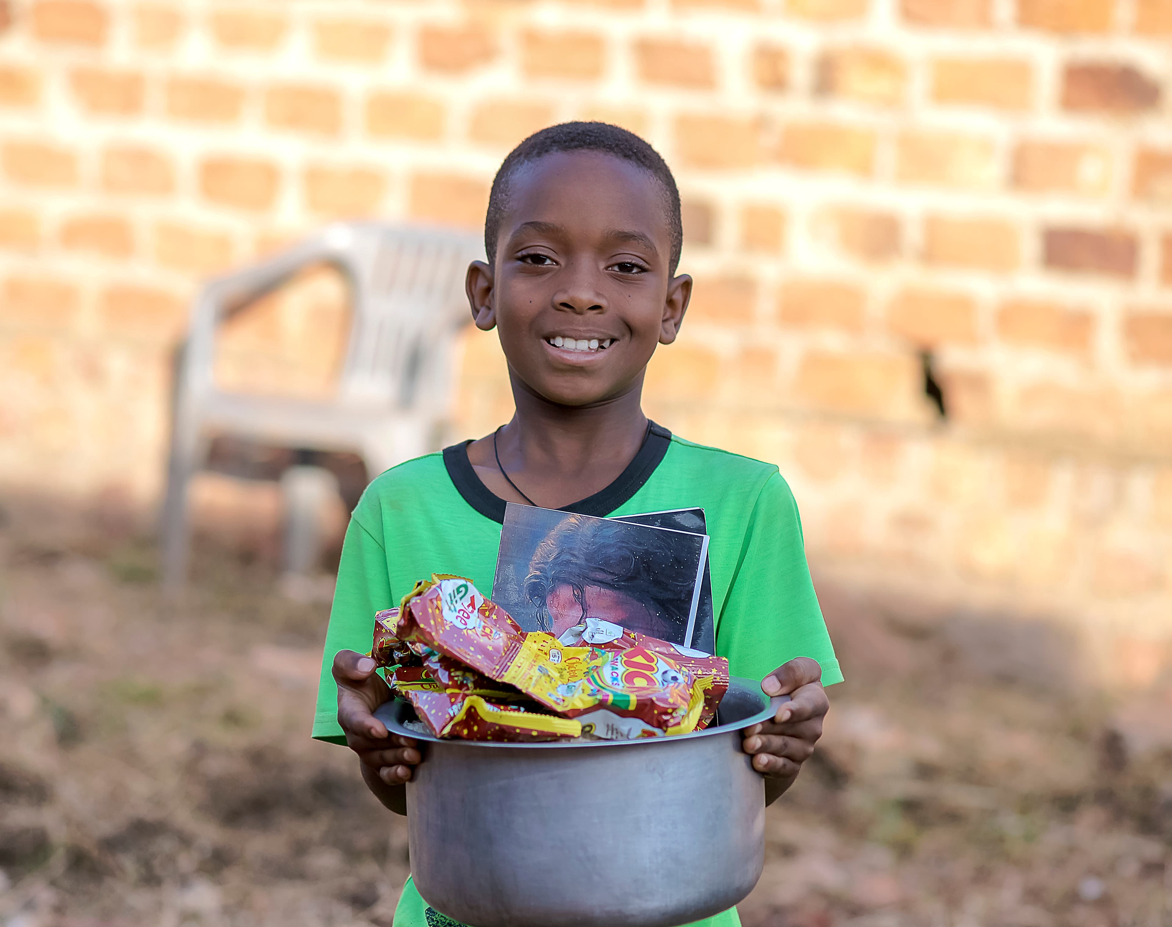Smiling boy holding a metal bowl filled with snack packets and treats
