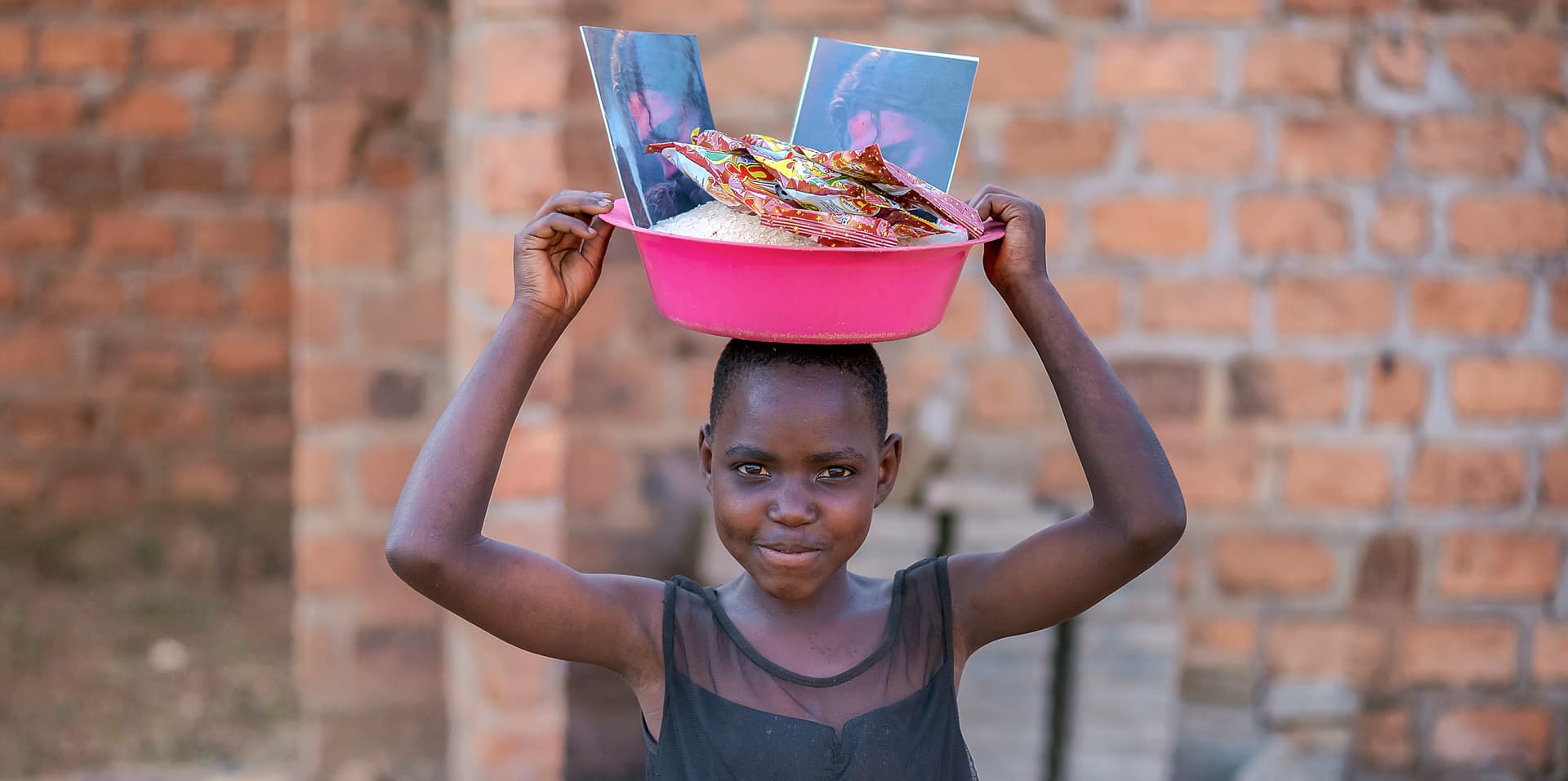 Girl carrying a pink basin of food items on her head outdoors