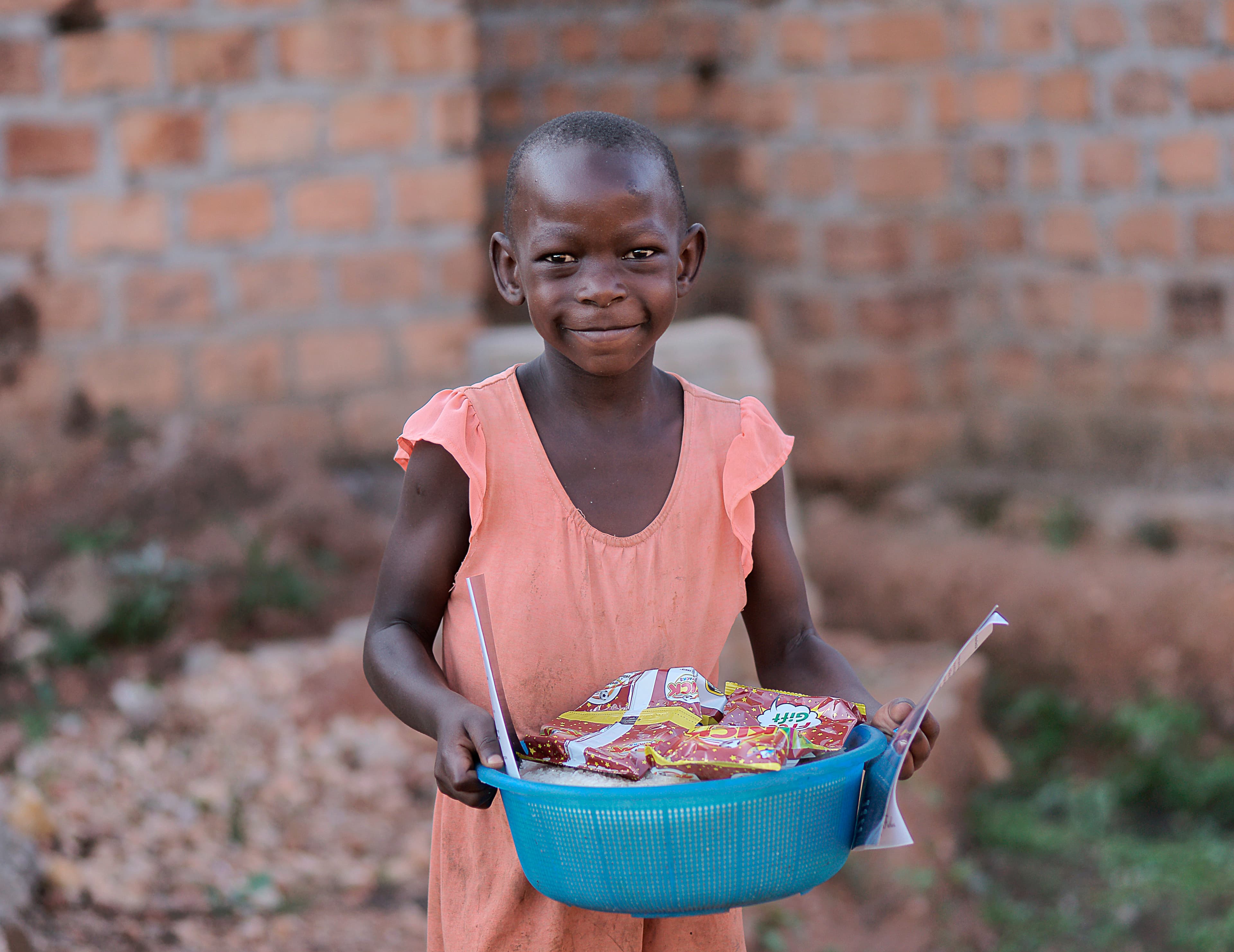 Girl in a peach dress holding a blue basin filled with food and supplies