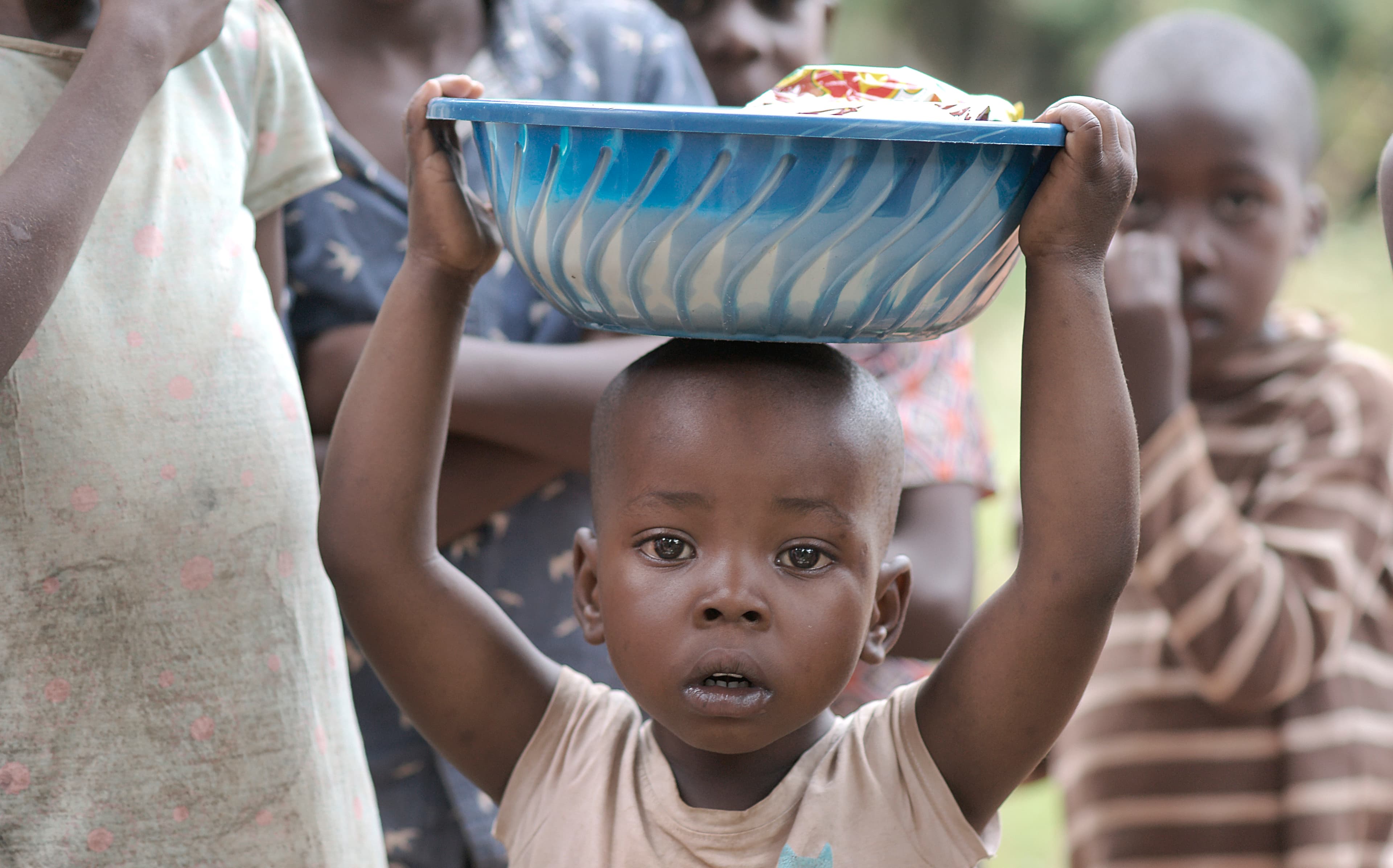 Woman carries a young child while other children walk behind her on a dirt path.