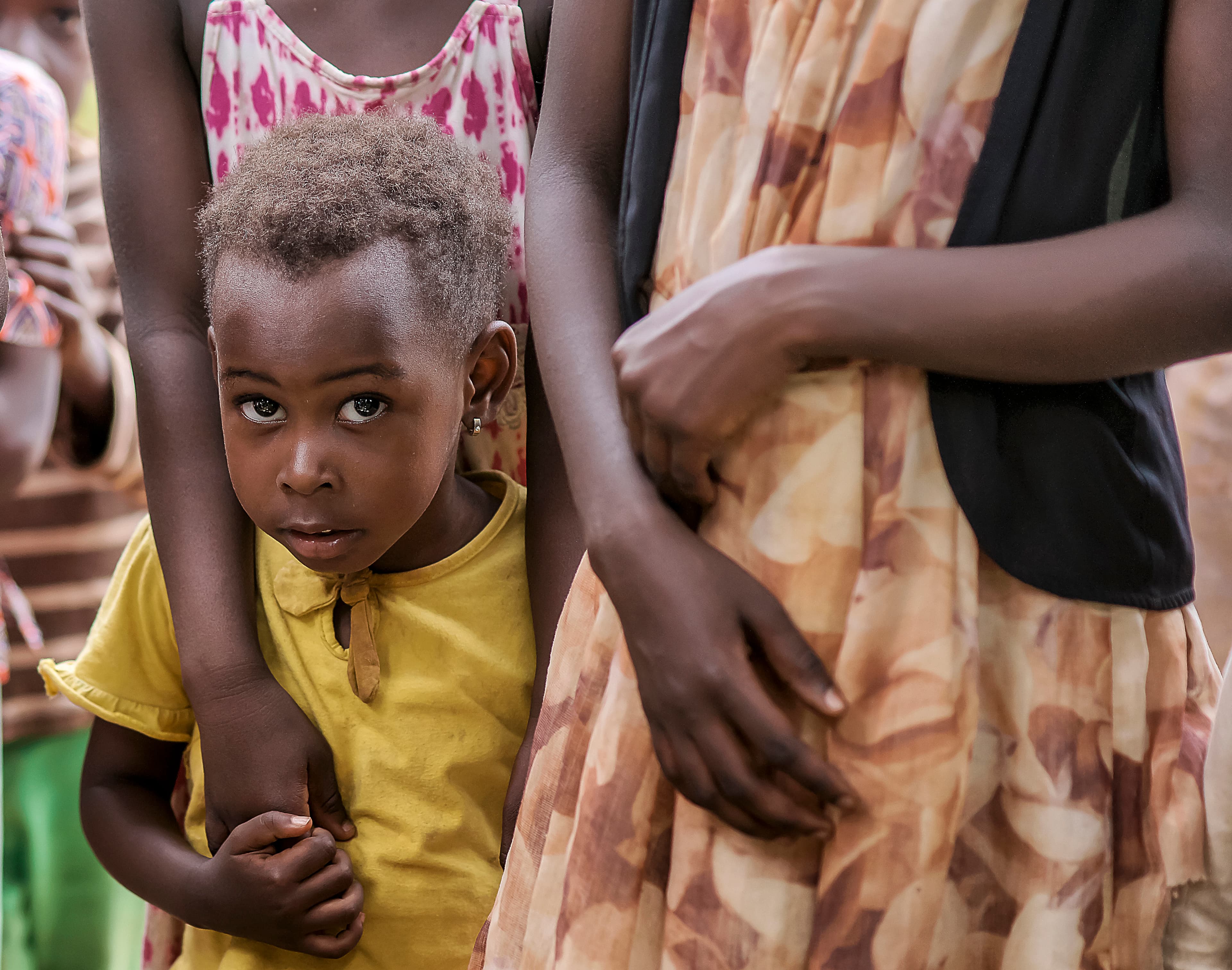 Young girl in a yellow shirt holds hands with an elderly woman in a patterned dress.
