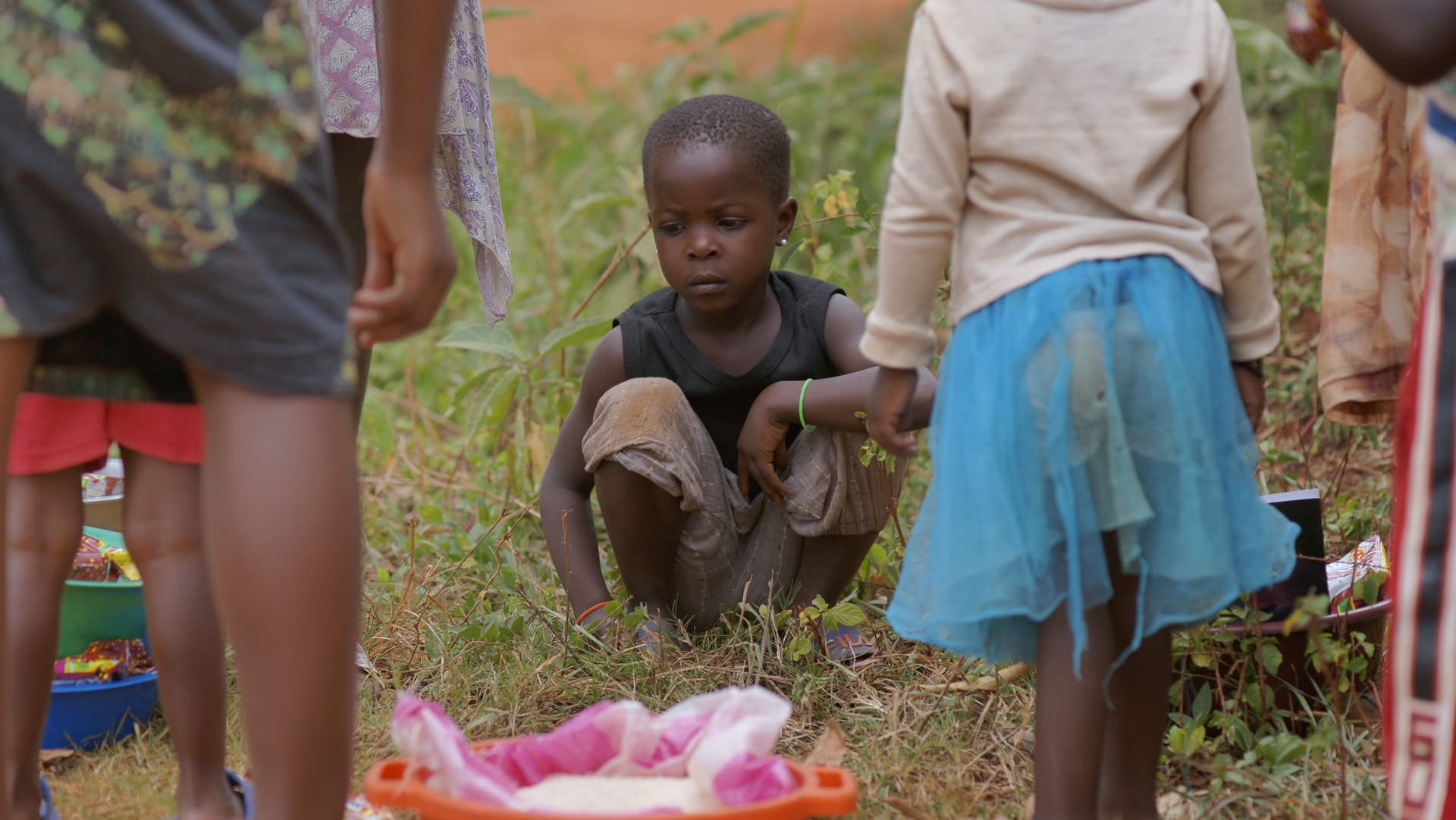 Children gather around a pink container set on the grass outdoors.