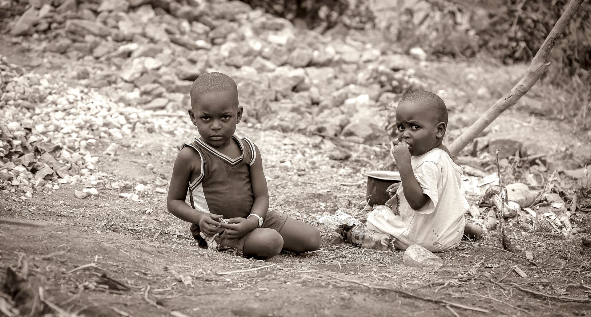 Black-and-white photo of two young children sitting together on rocky ground.