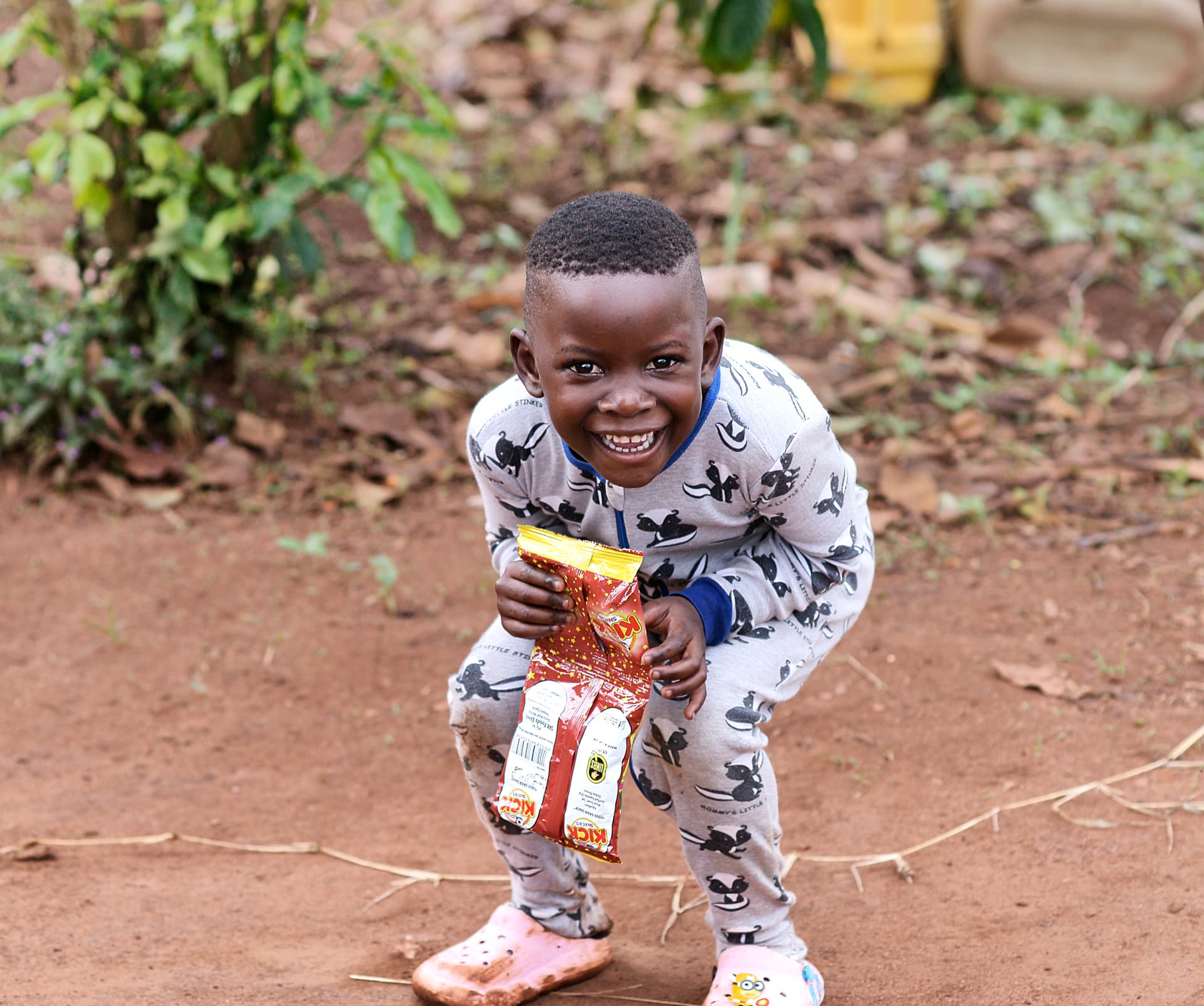 Boy in pajama-print clothing crouches while holding a food package.