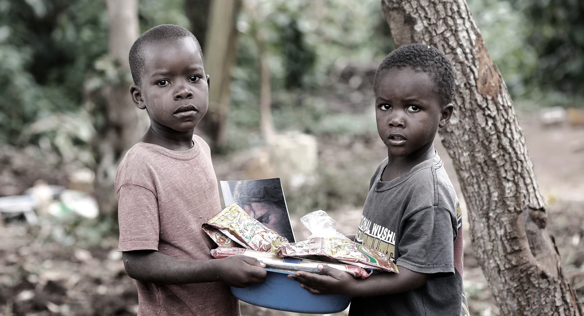 Black-and-white photo of two boys standing close together holding food packages.