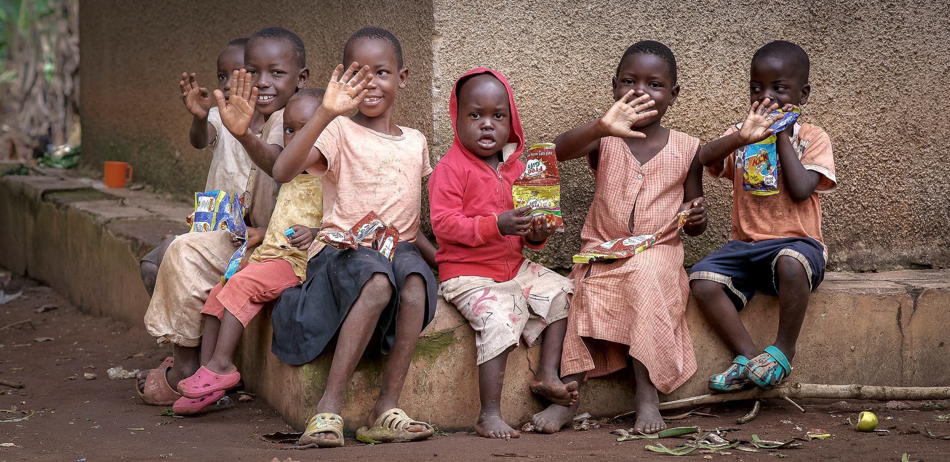 A group of children sit together on a stone ledge, some holding gospel tract booklets.