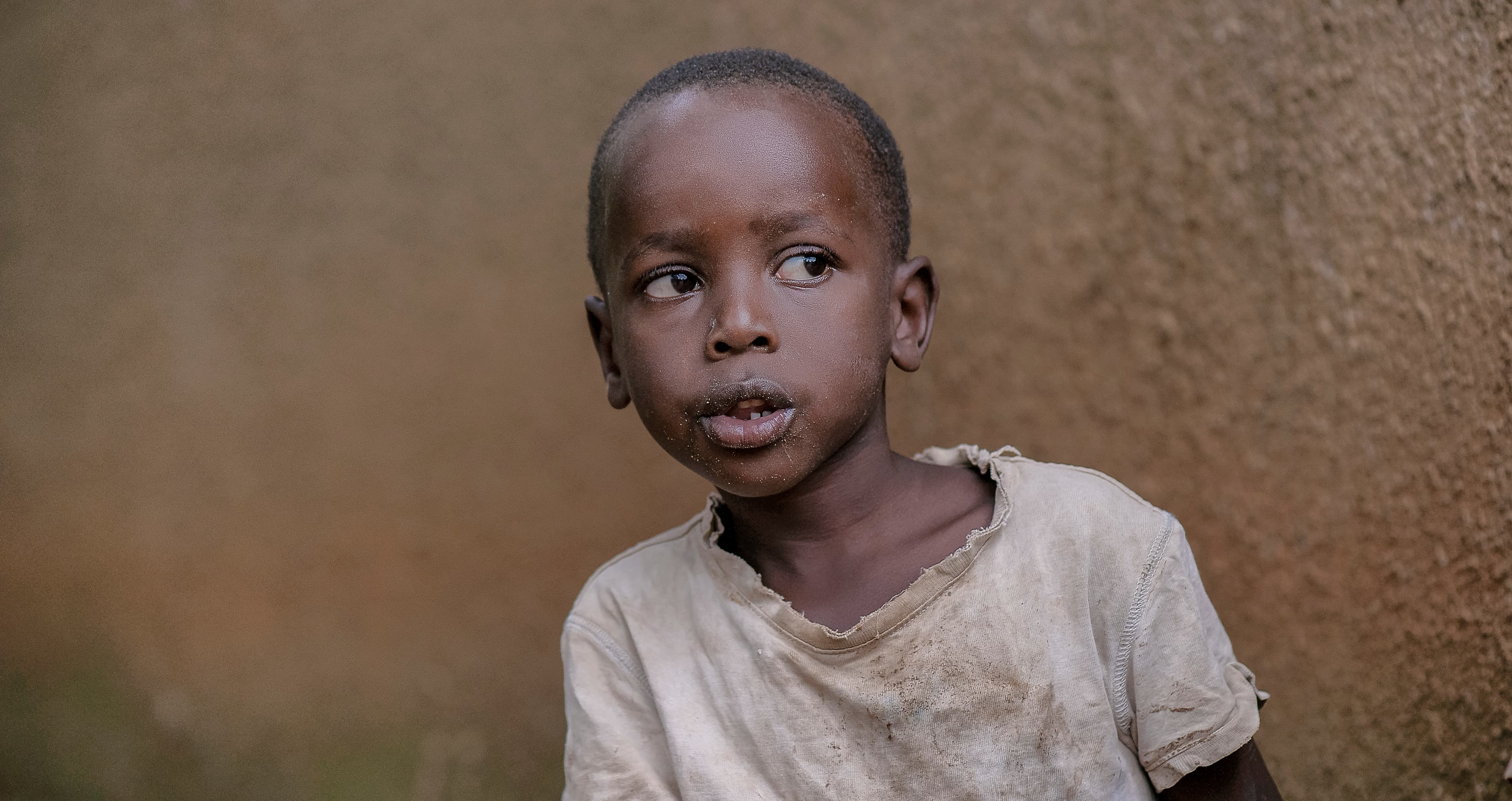 Close portrait of a young boy standing against a tan wall.