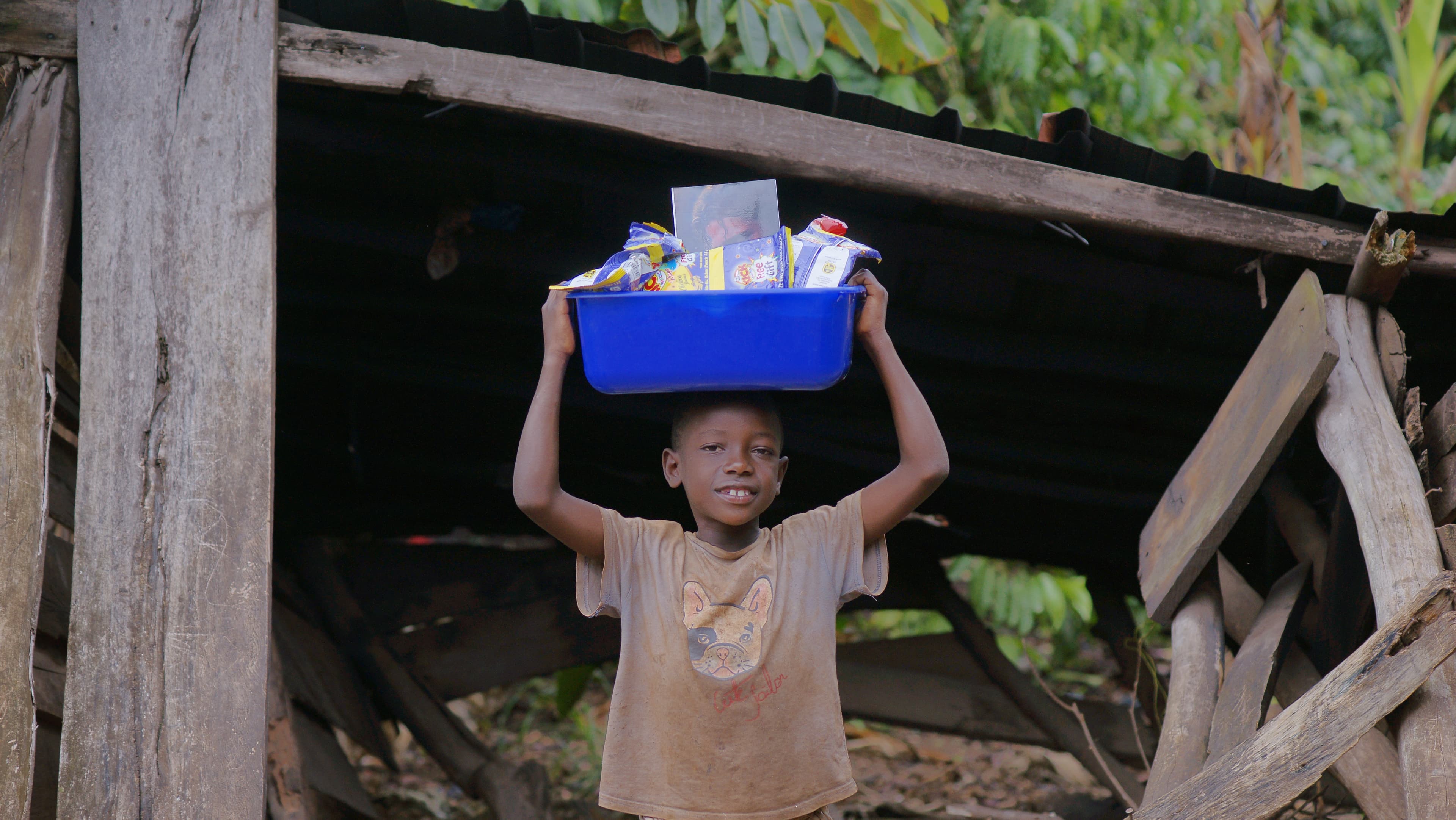 Boy stands under a wooden structure holding a blue food package.