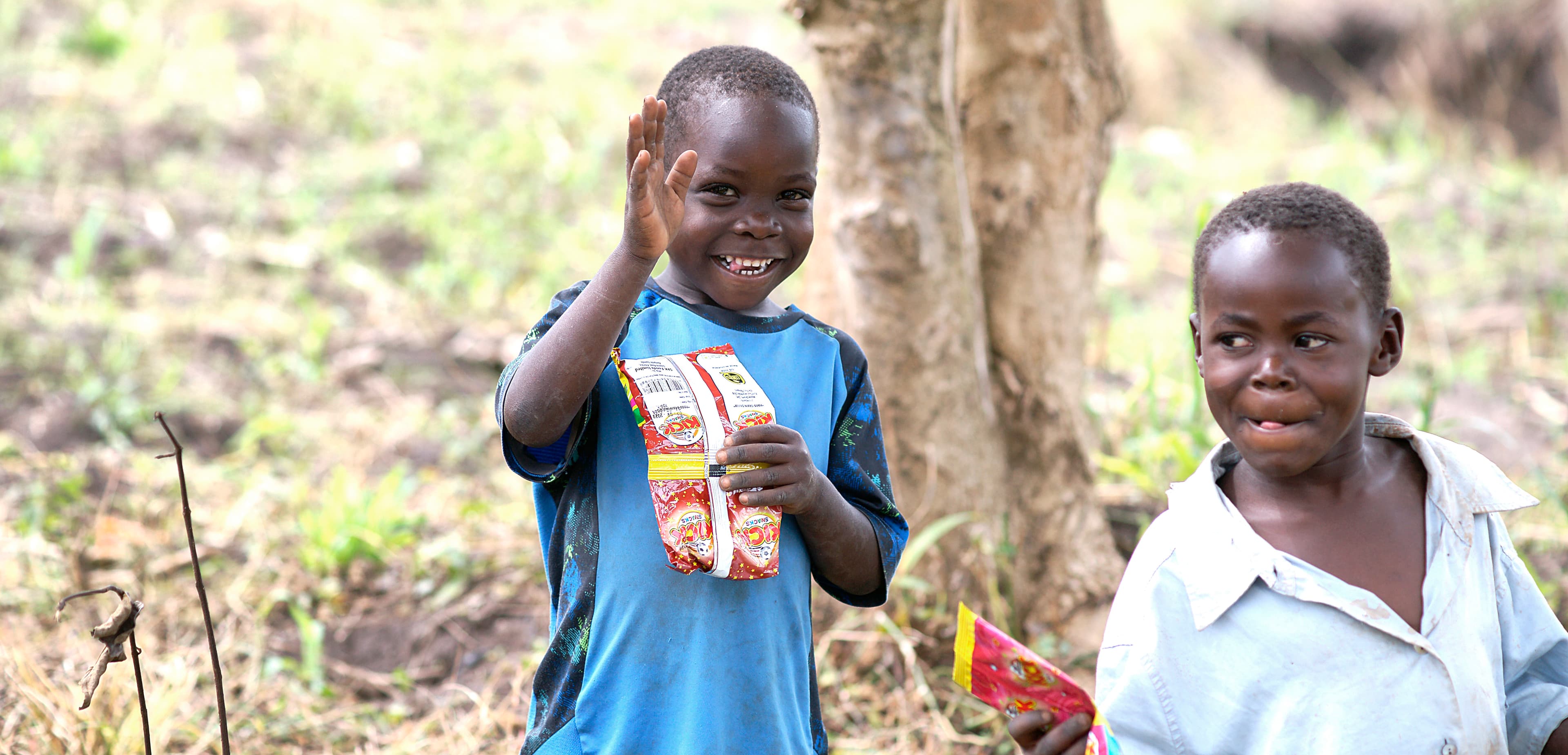 Two smiling boys stand together, one holding a food package.