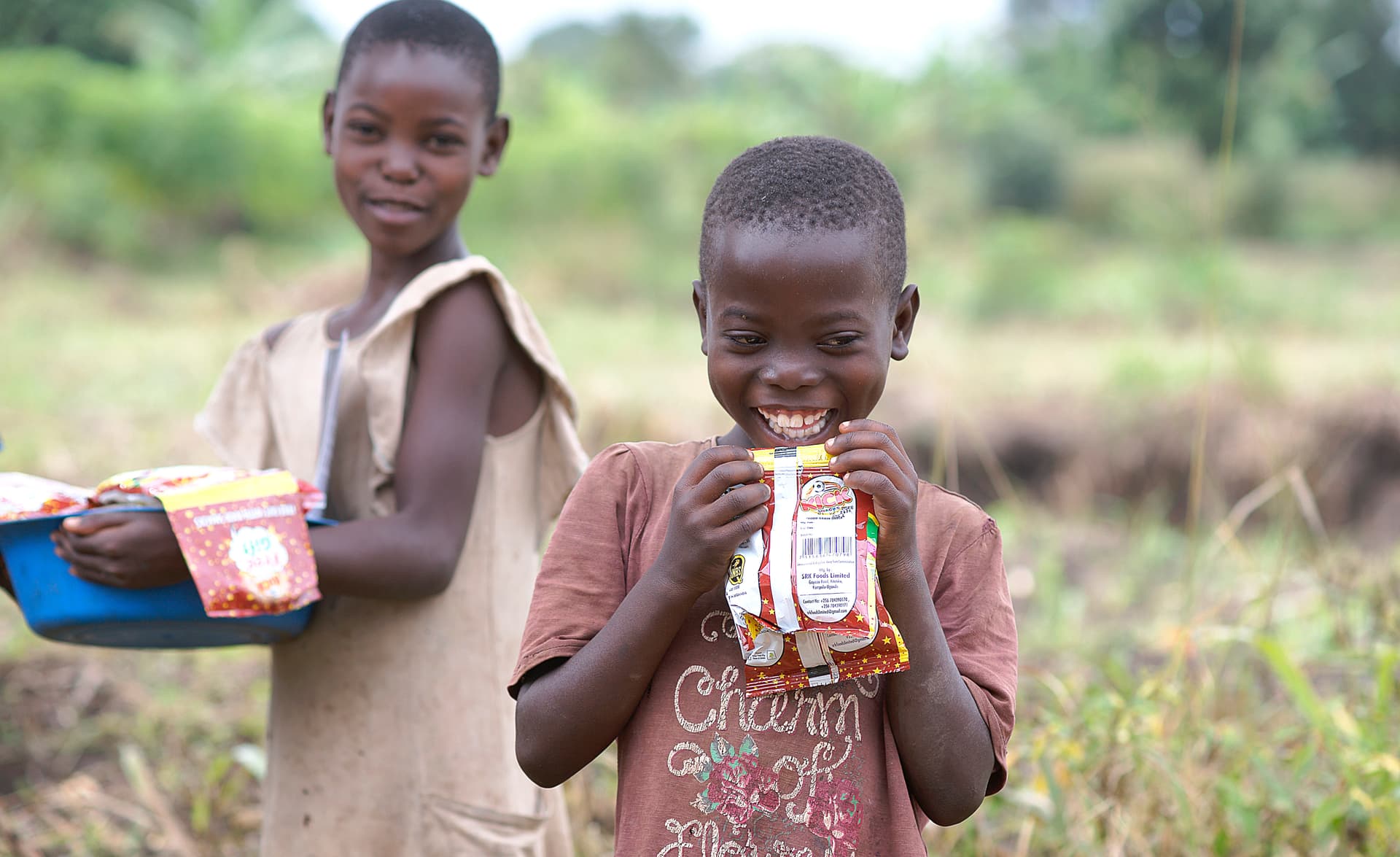 Two boys stand together eating snack packages.
